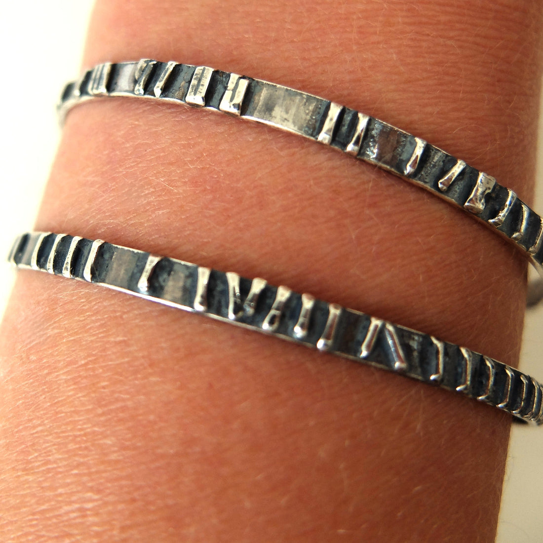Close-up of a person's wrist wearing two silver textured bracelets.