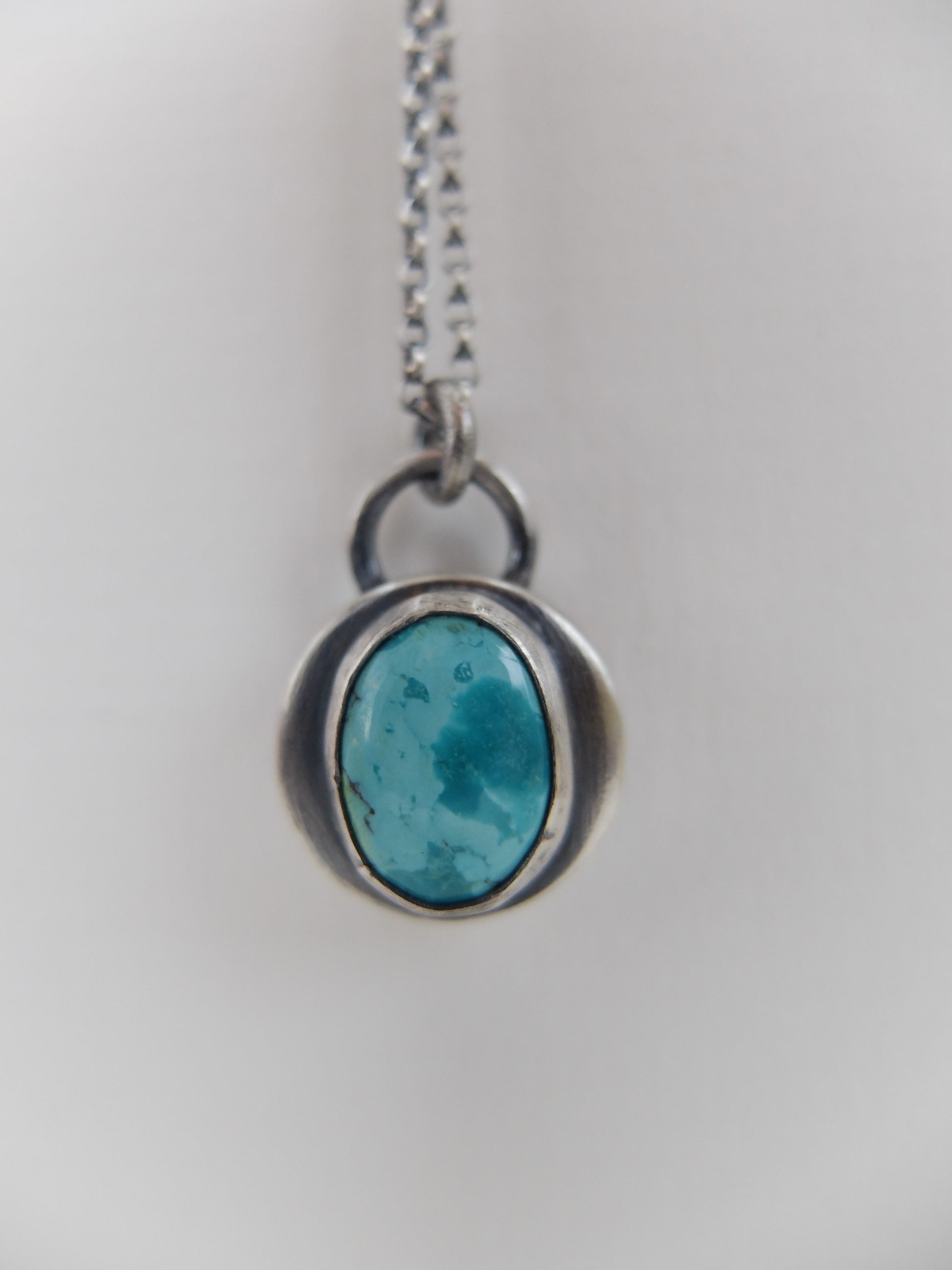 Turquoise pendant on a silver chain against a light gray background