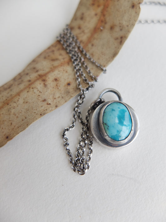 Turquoise stone pendant on a chain with a wooden background