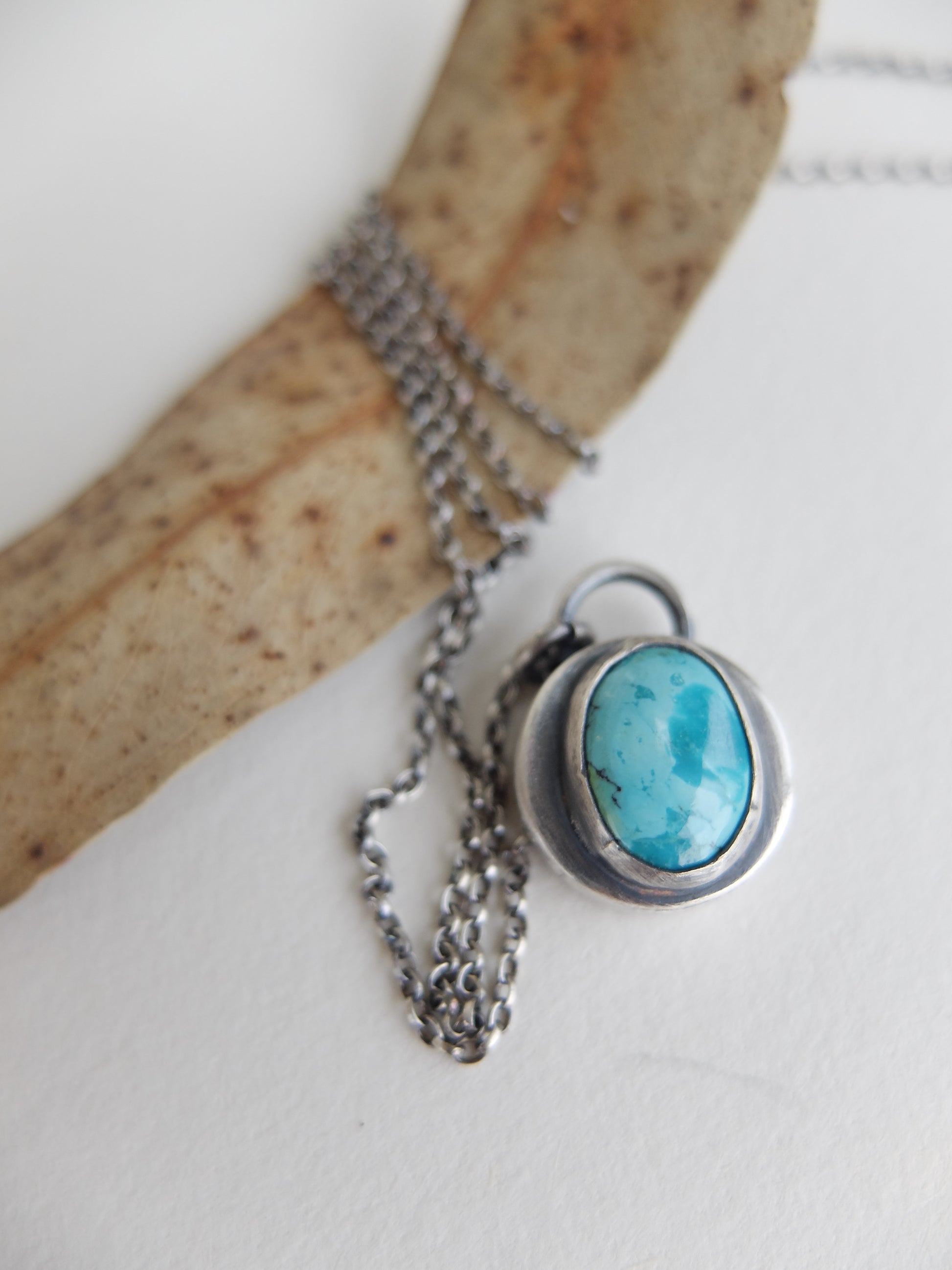 Turquoise stone pendant on a chain against a white background