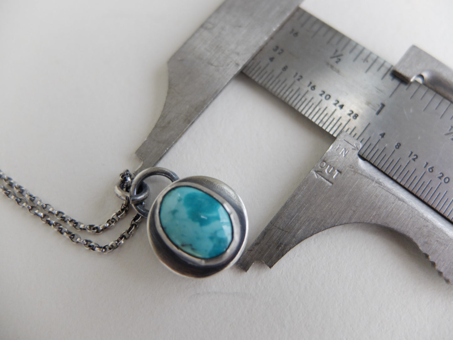 Necklace with turquoise pendant next to a ruler on a white background