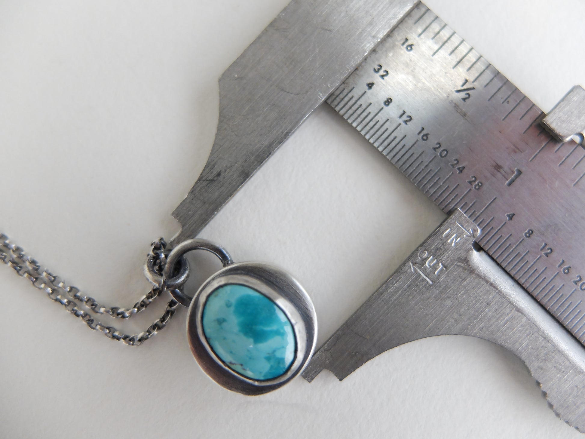 Necklace with a turquoise stone being measured by a caliper on a white background