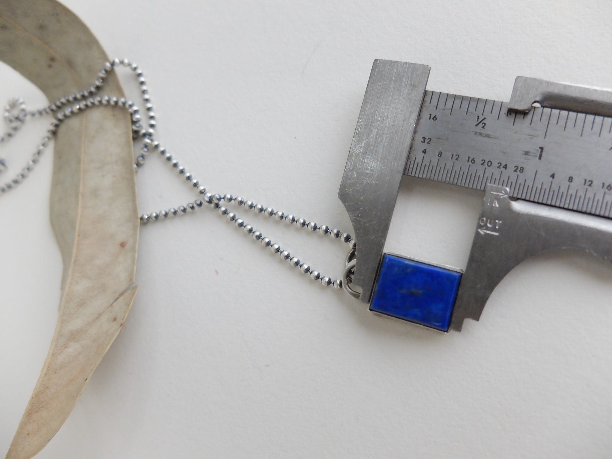 Metallic necklace with a caliper measuring its length on a white background