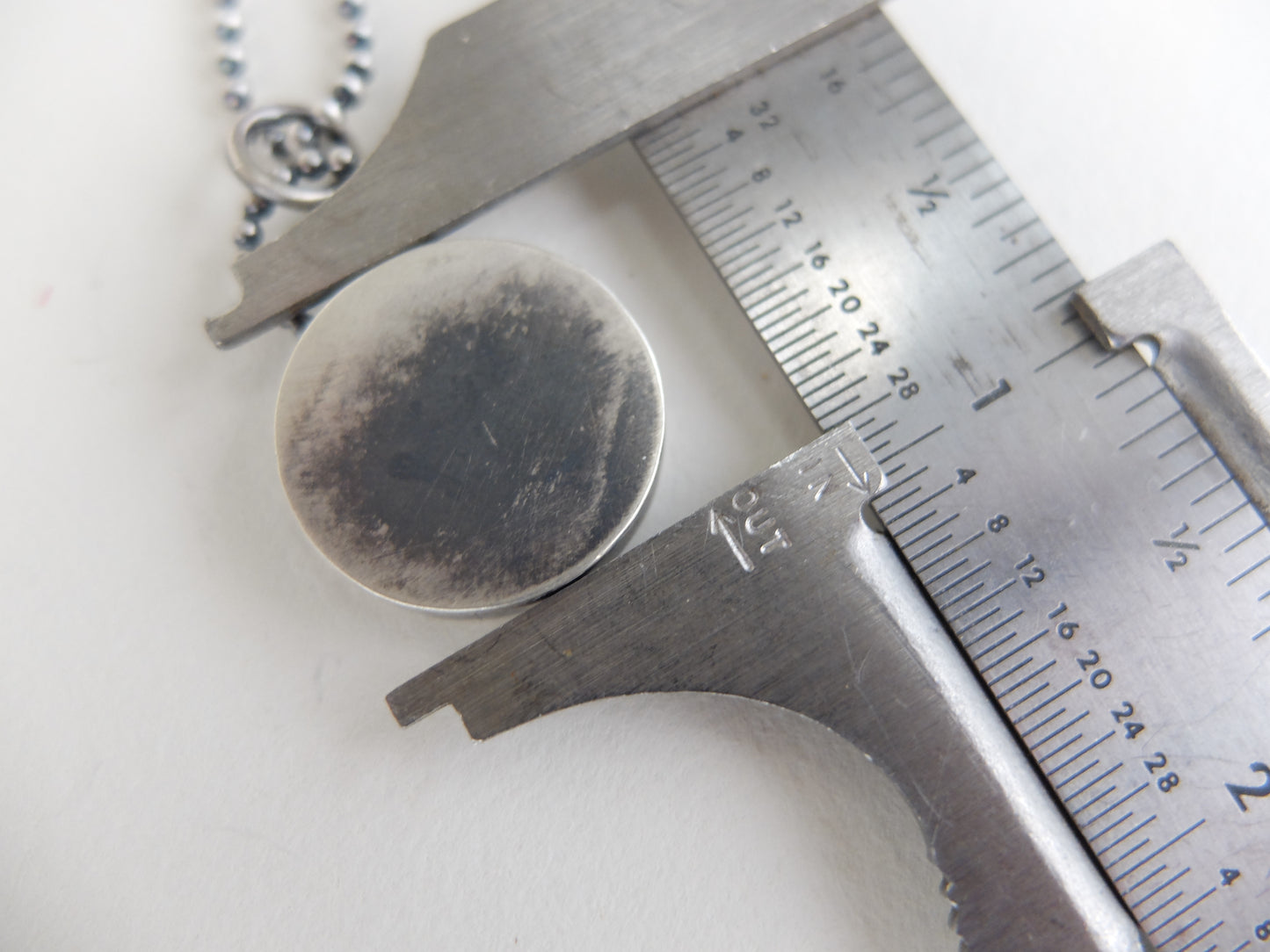 Close-up of a silver pendant being measured with a caliper on a white background