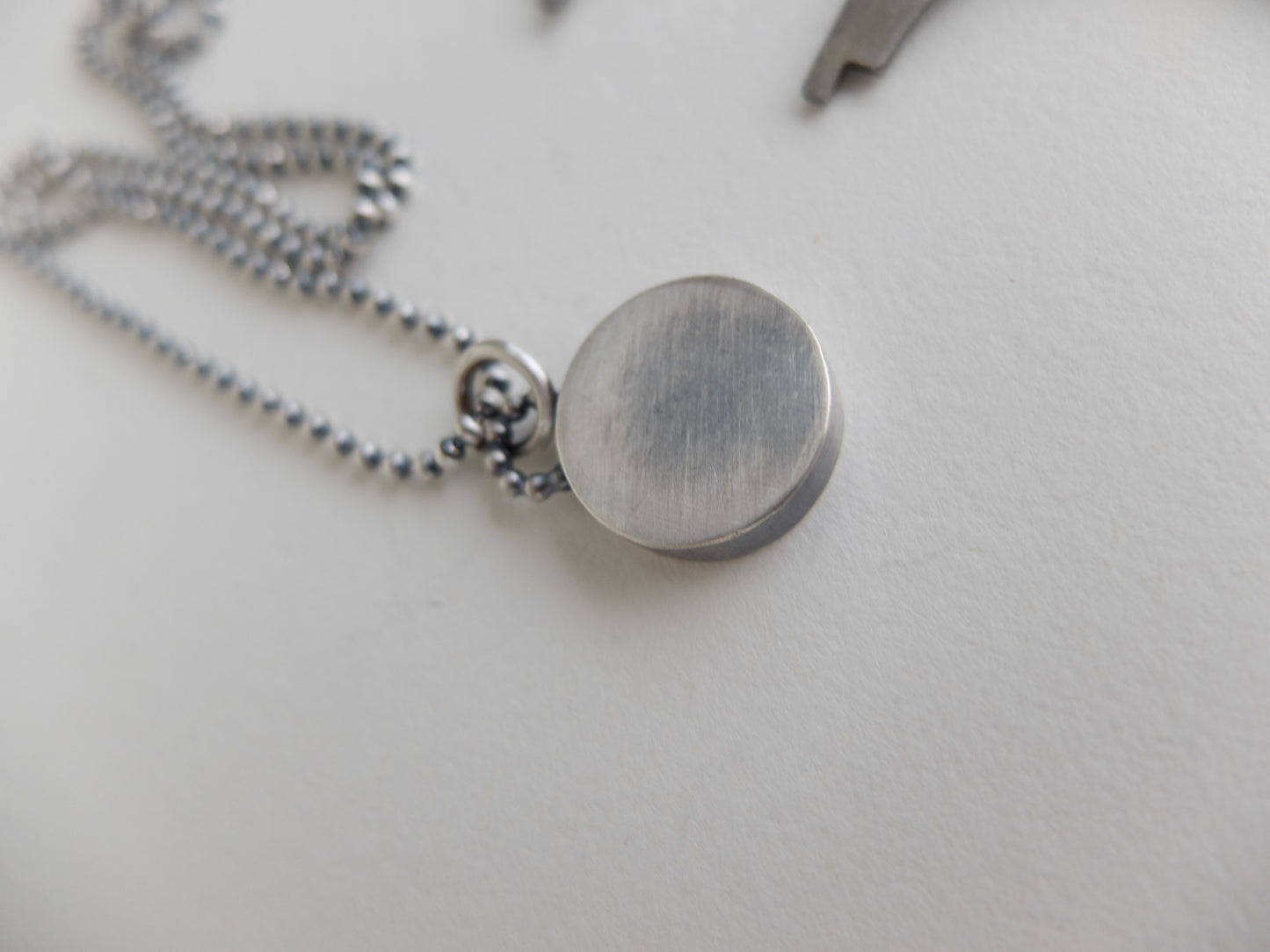 Close-up of a silver necklace with a round pendant on a light gray background