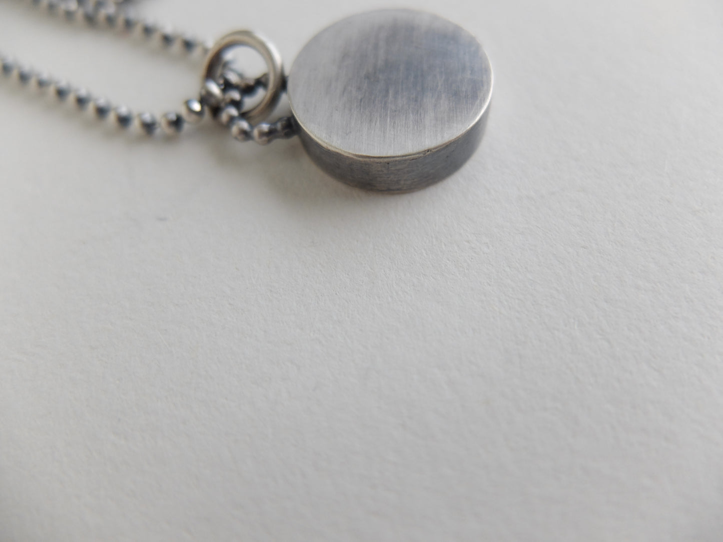Close-up of a silver pendant on a chain against a light gray background