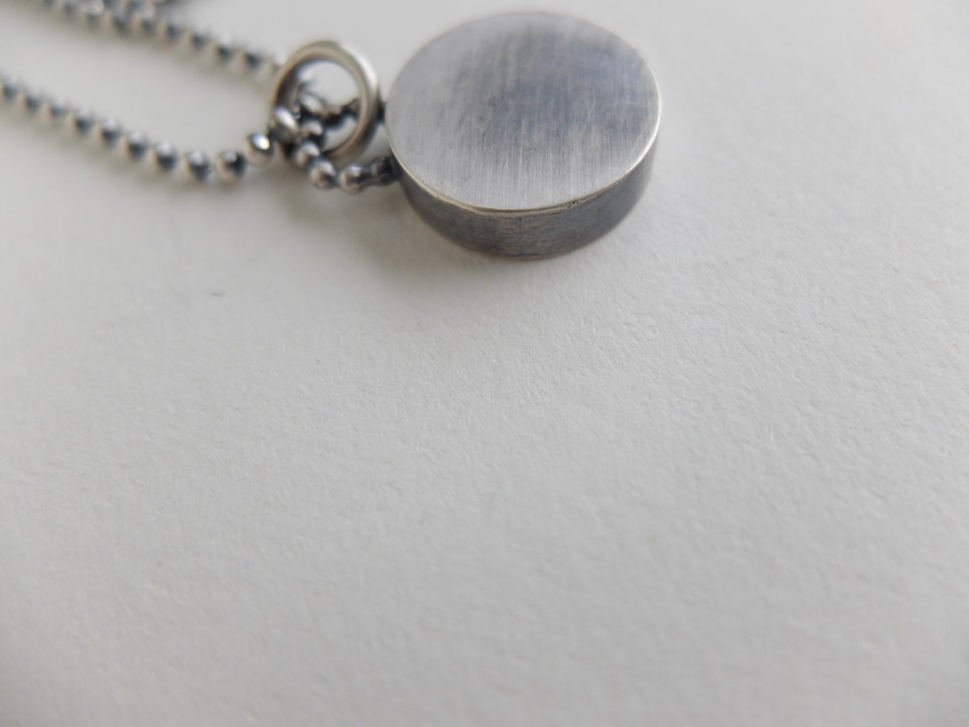 Close-up of a silver pendant on a chain against a light gray background