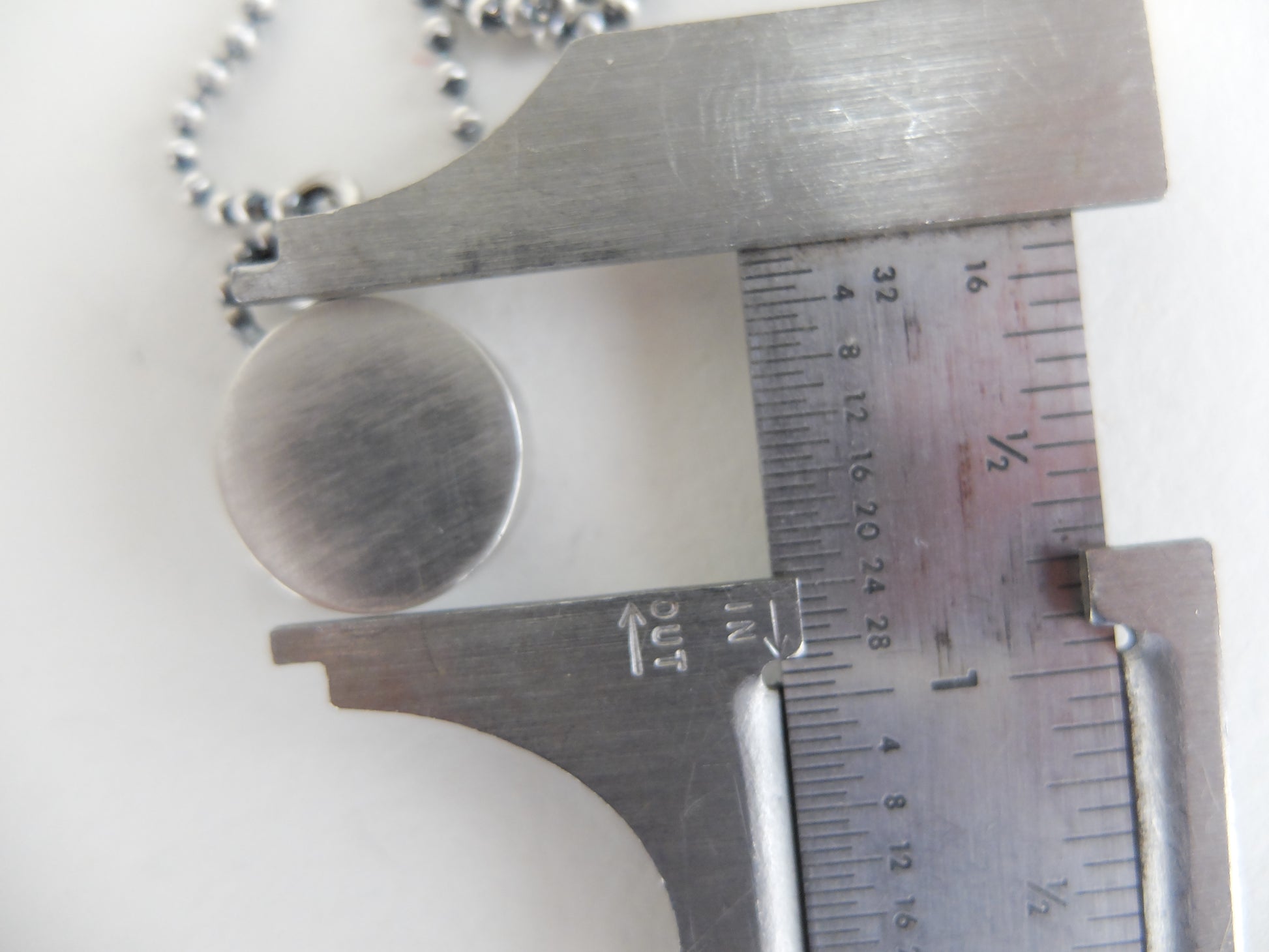 Metallic pendant on a chain with a caliper measuring its size against a white background