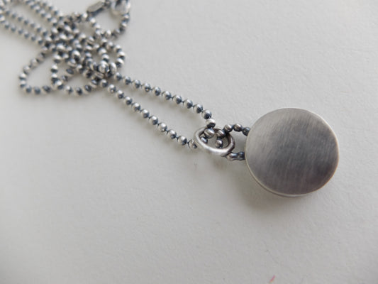 Silver necklace with a round pendant on a light gray background