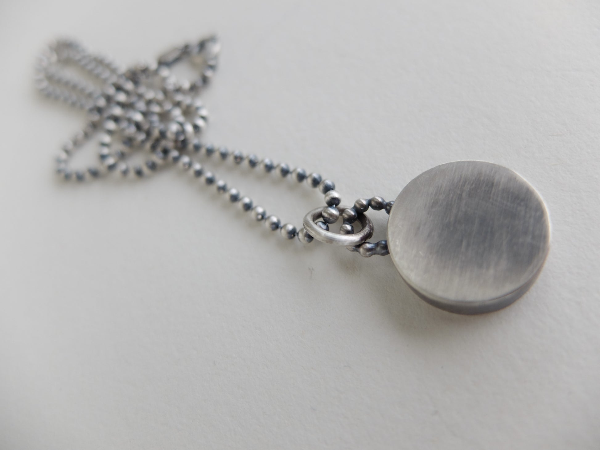 Silver necklace with a round pendant on a light gray background