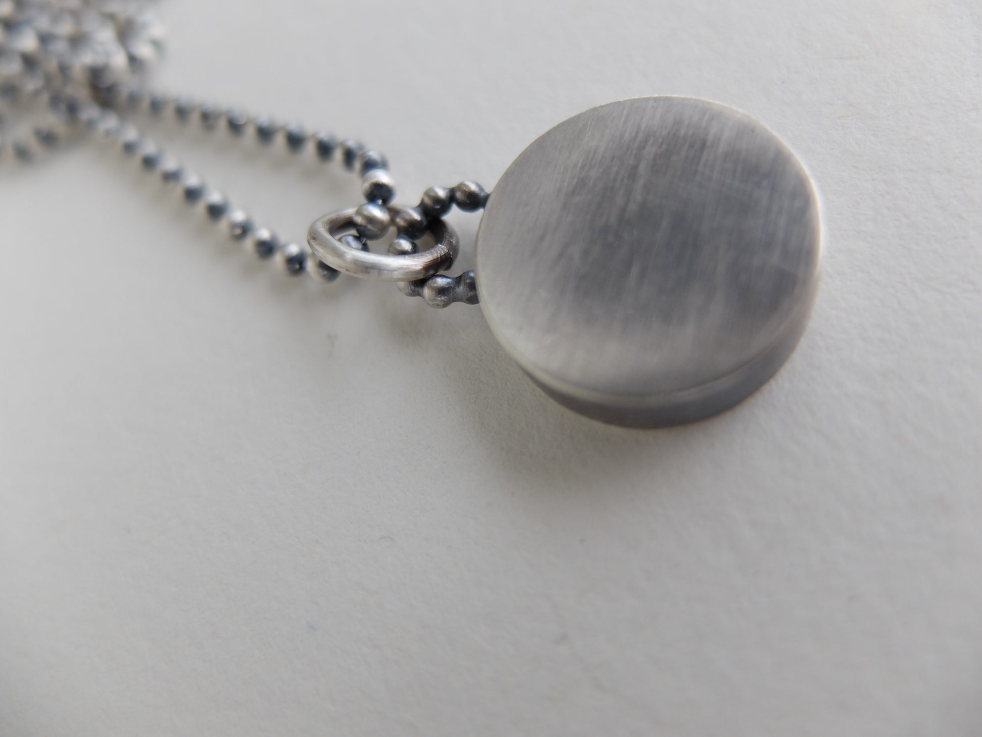 Silver necklace with a round pendant on a light gray background