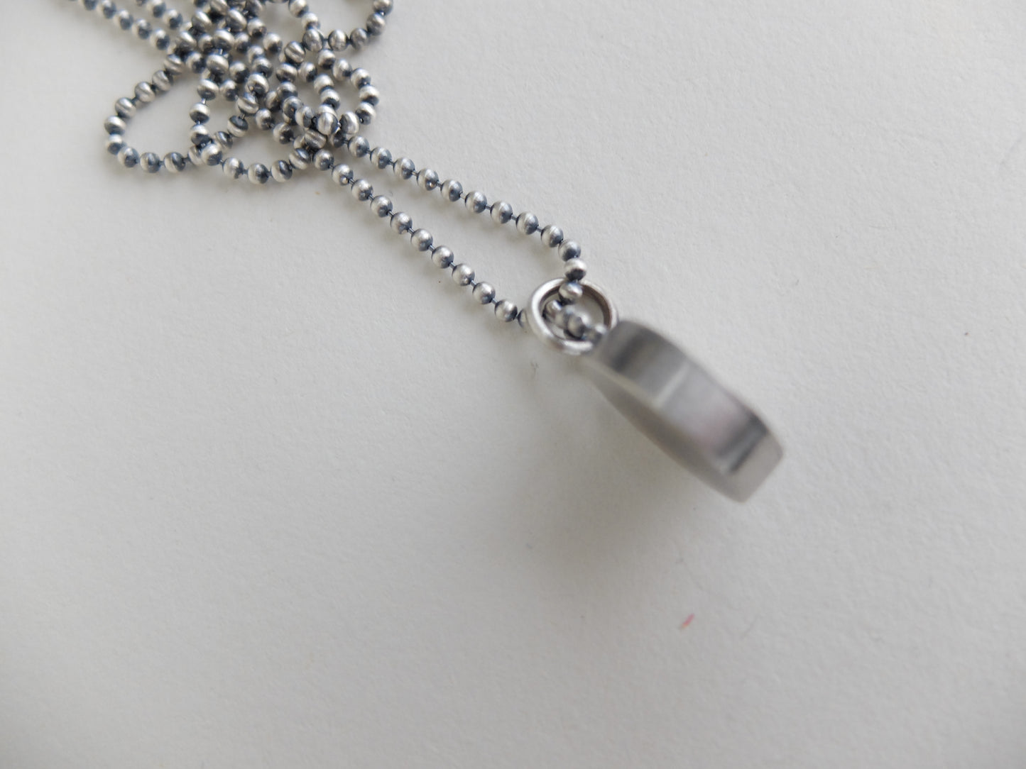 Silver necklace with a cylindrical pendant on a light gray background