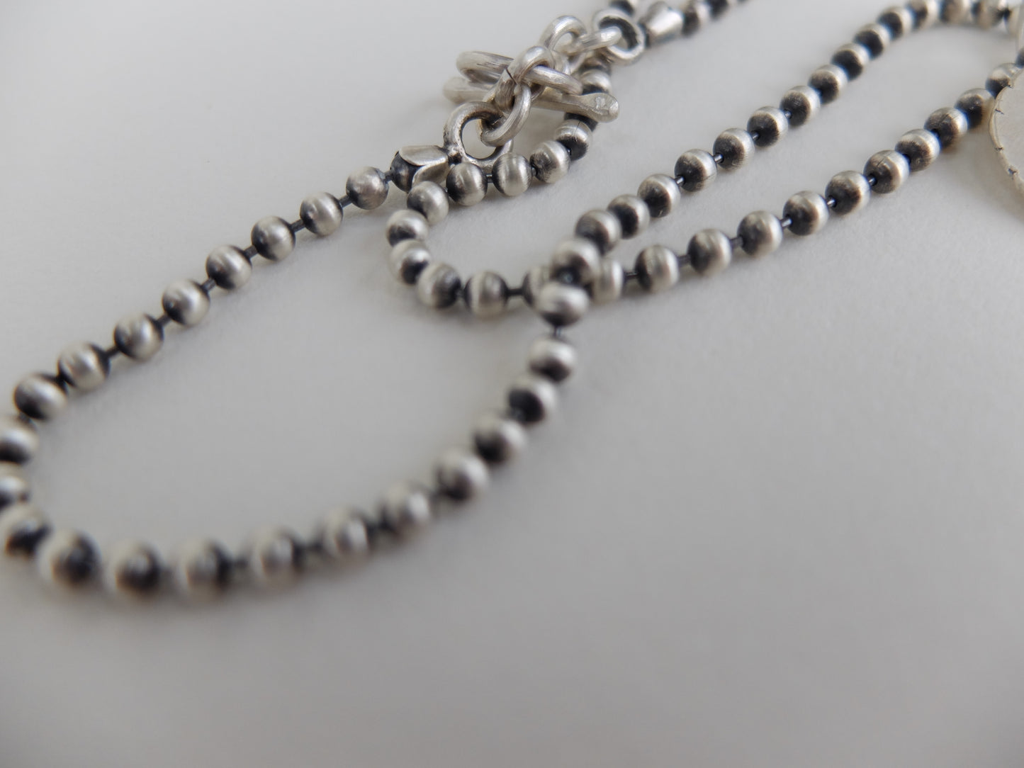 Close-up of a silver beaded necklace on a light gray background
