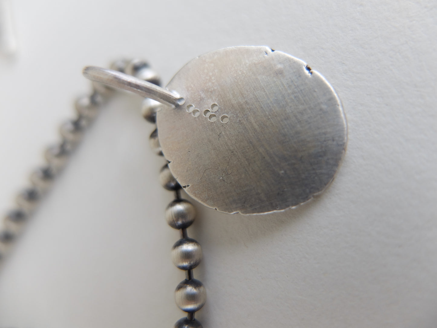 Close-up of a silver necklace with a round pendant on a light background