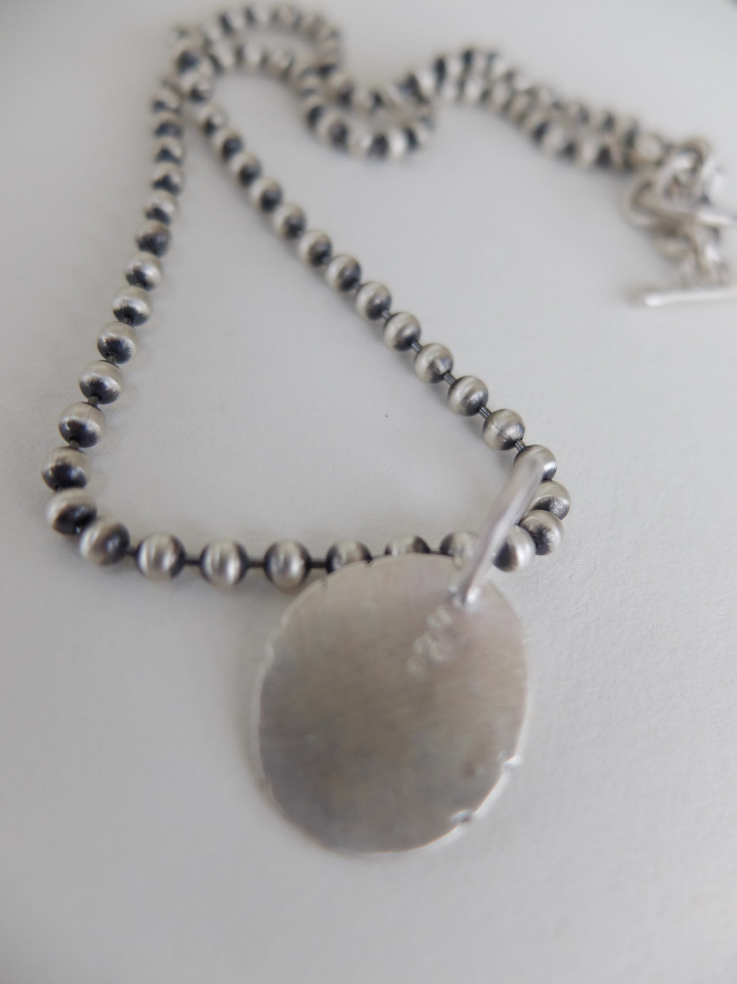 Silver necklace with a round pendant on a white background