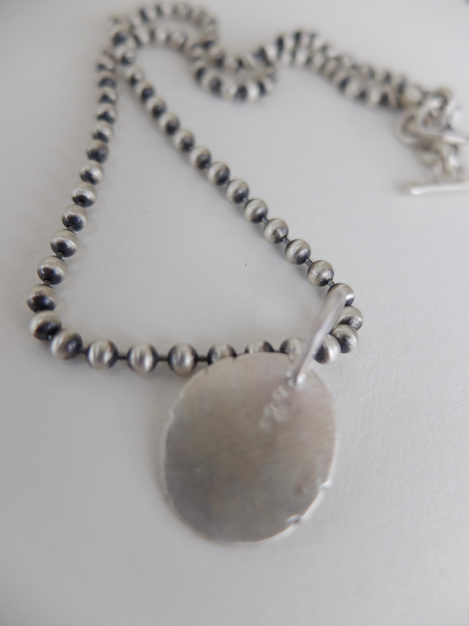Silver necklace with a round pendant on a white background