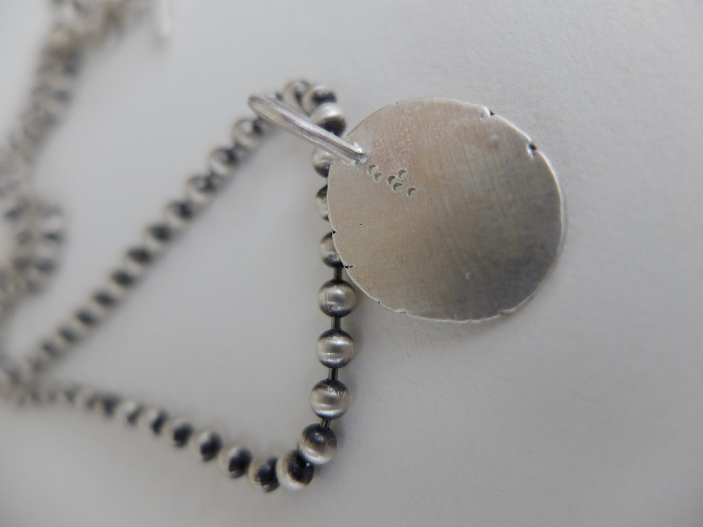 Silver necklace with a round pendant on a light gray background