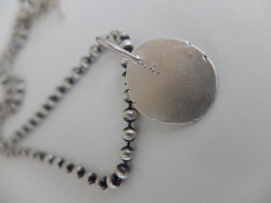 Silver necklace with a round pendant on a light gray background