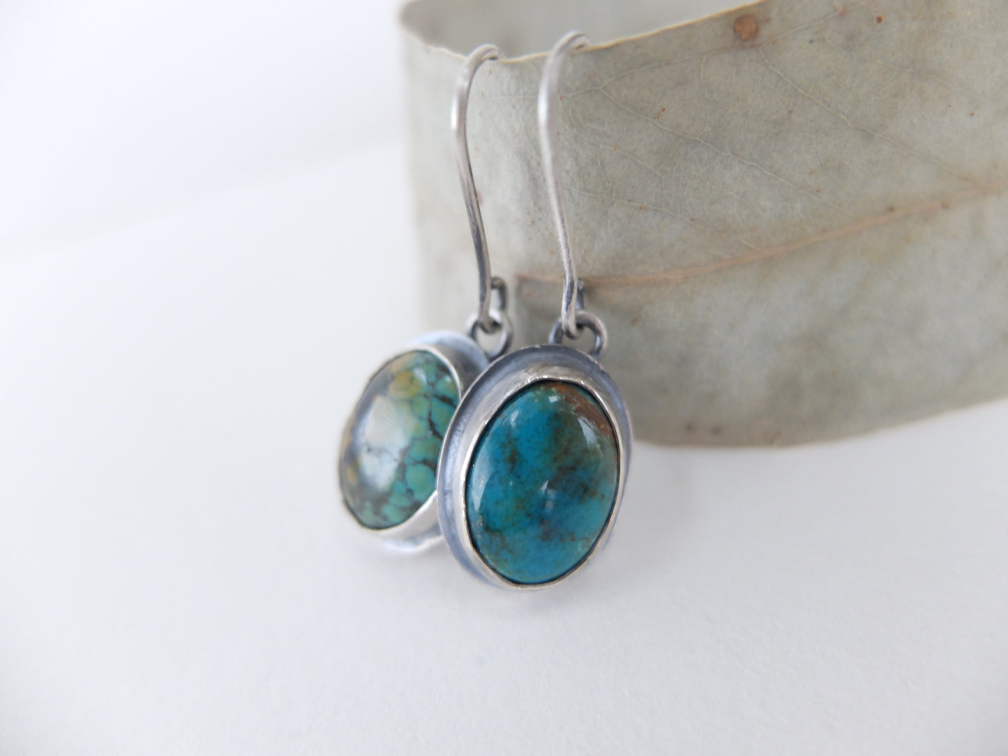 Turquoise stone earrings on silver hooks against a white background