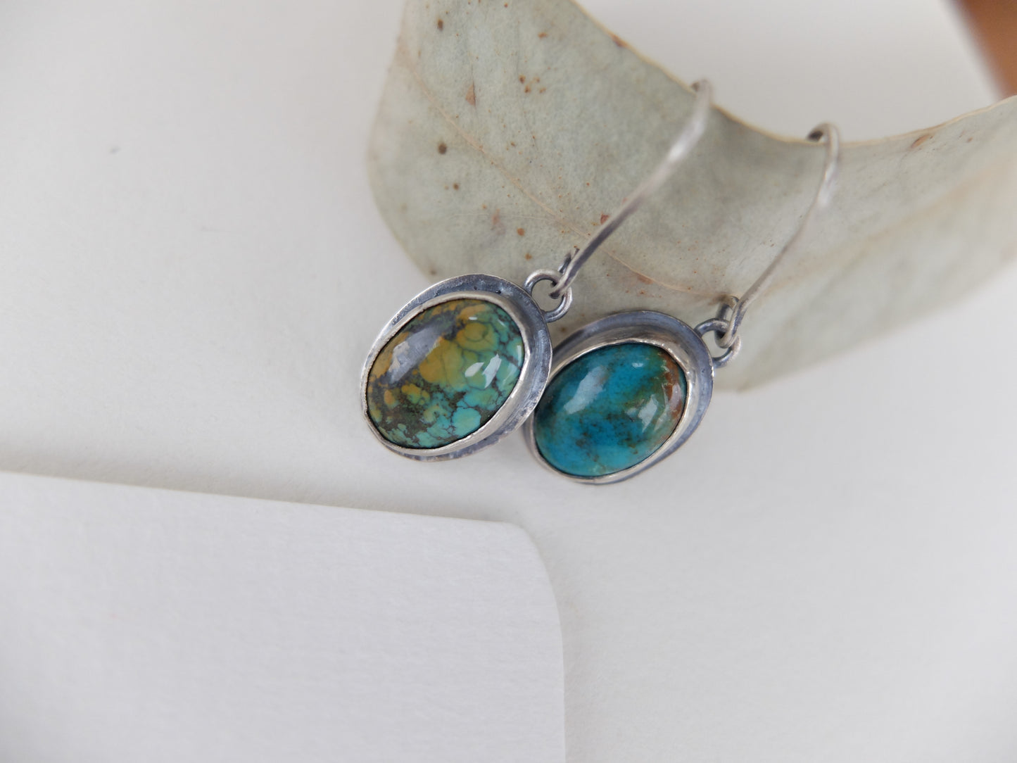 Turquoise stone earrings on a white surface with a leaf