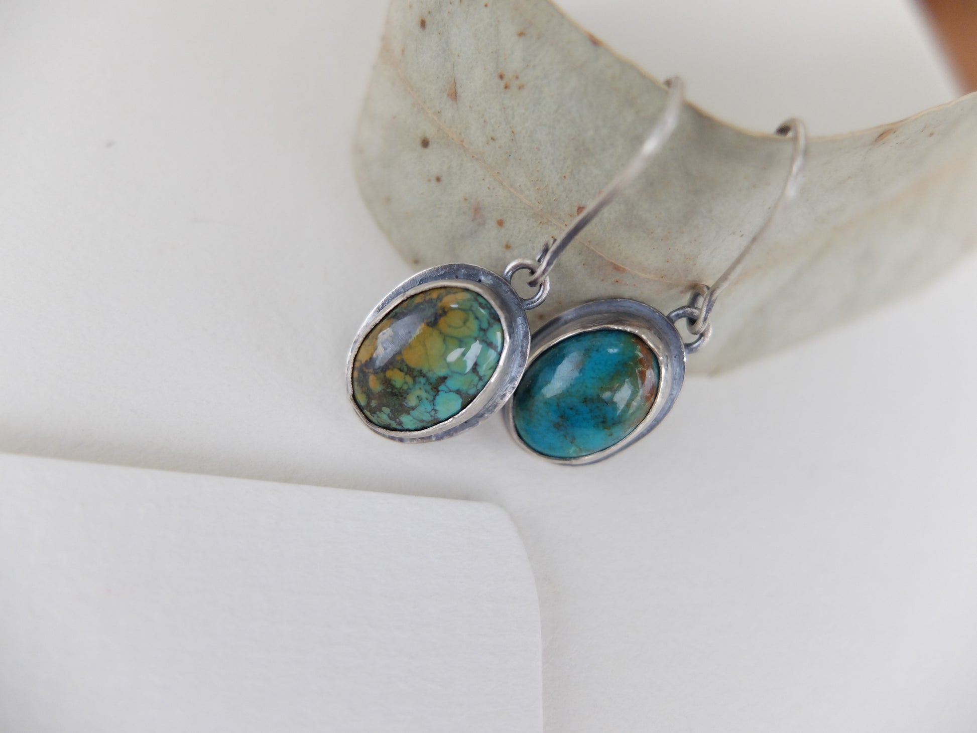 Turquoise stone earrings on a white surface with a leaf