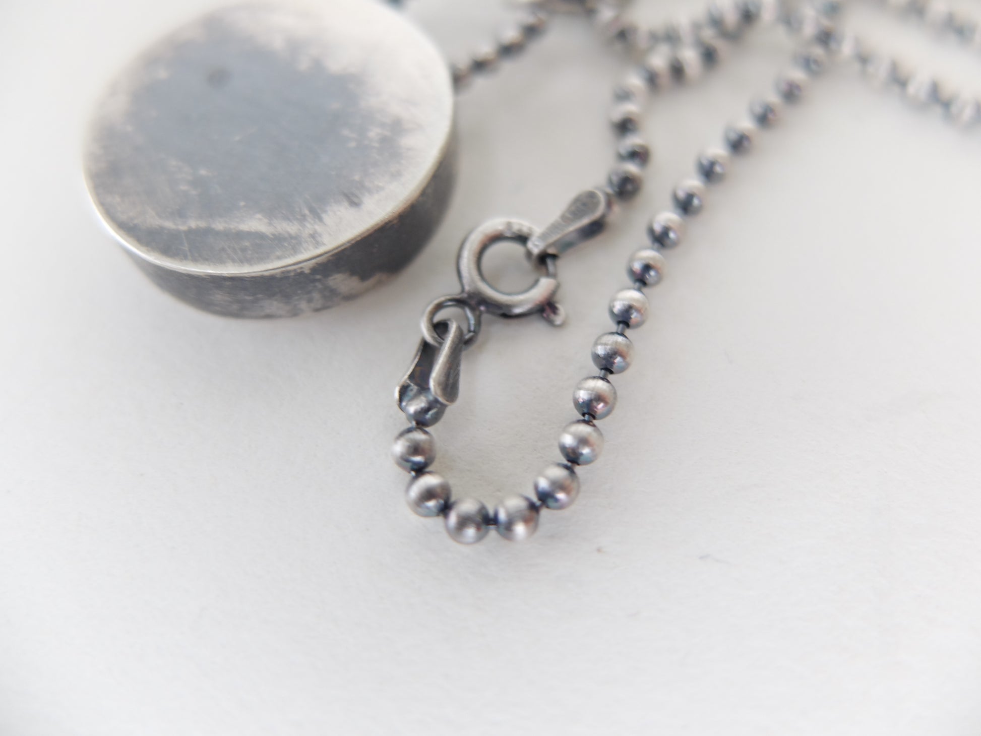 Close-up of a silver beaded necklace with clasp on a white background