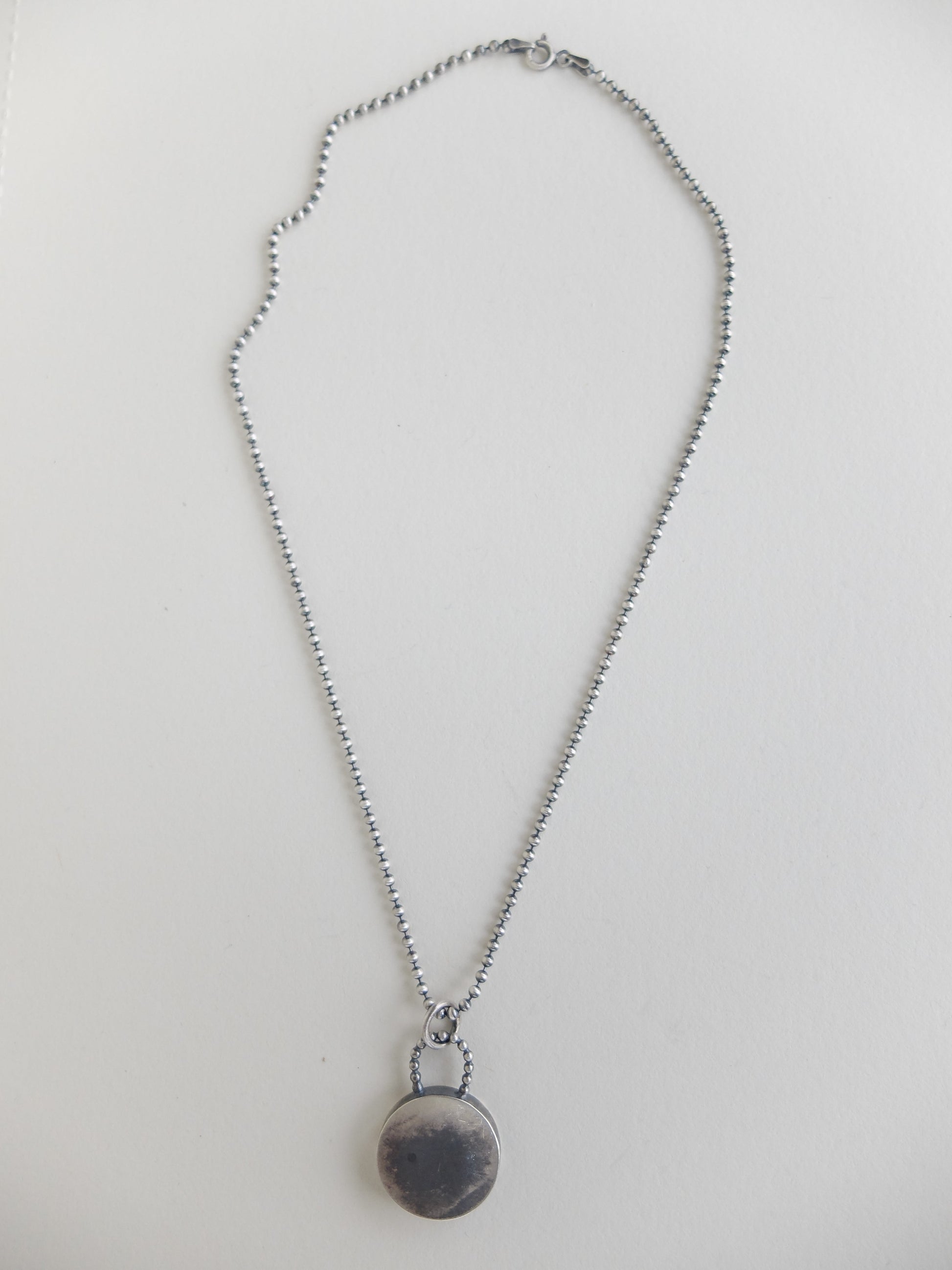 Silver chain with a round pendant on a light gray background