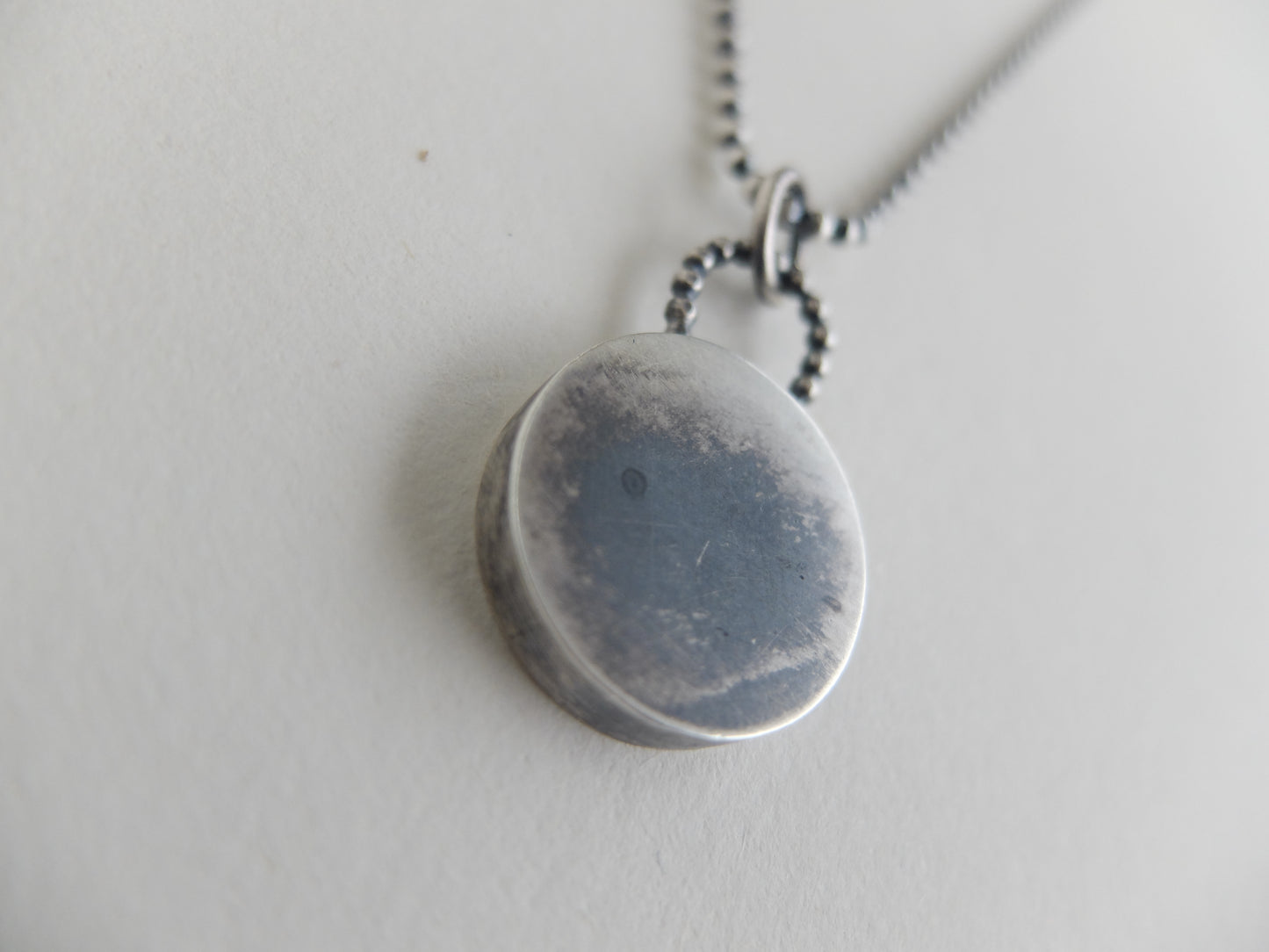 Silver necklace with a round pendant on a light gray background