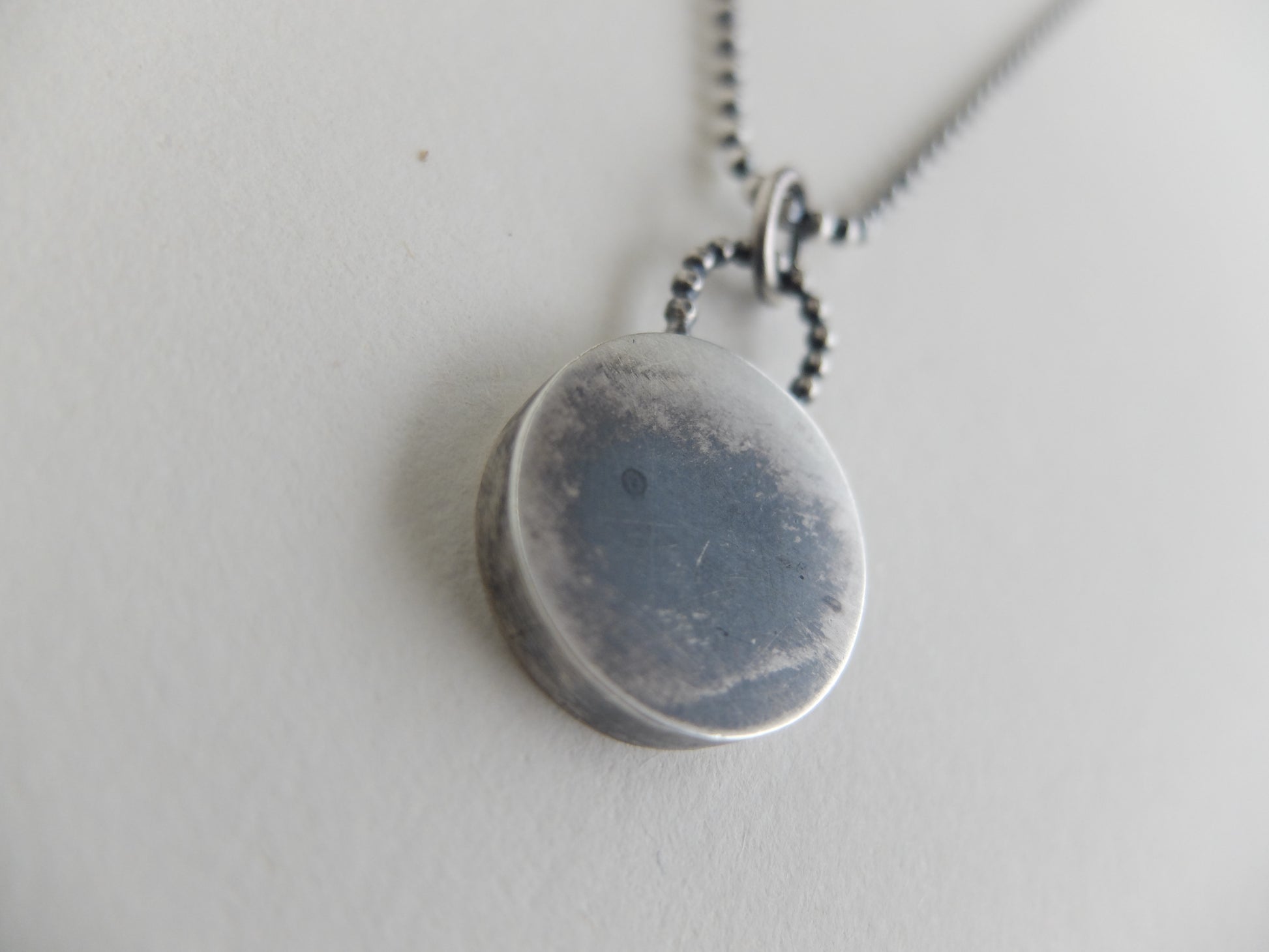 Silver necklace with a round pendant on a light gray background