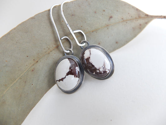 Pair of earrings with oval-shaped brown and white stones on a leaf background