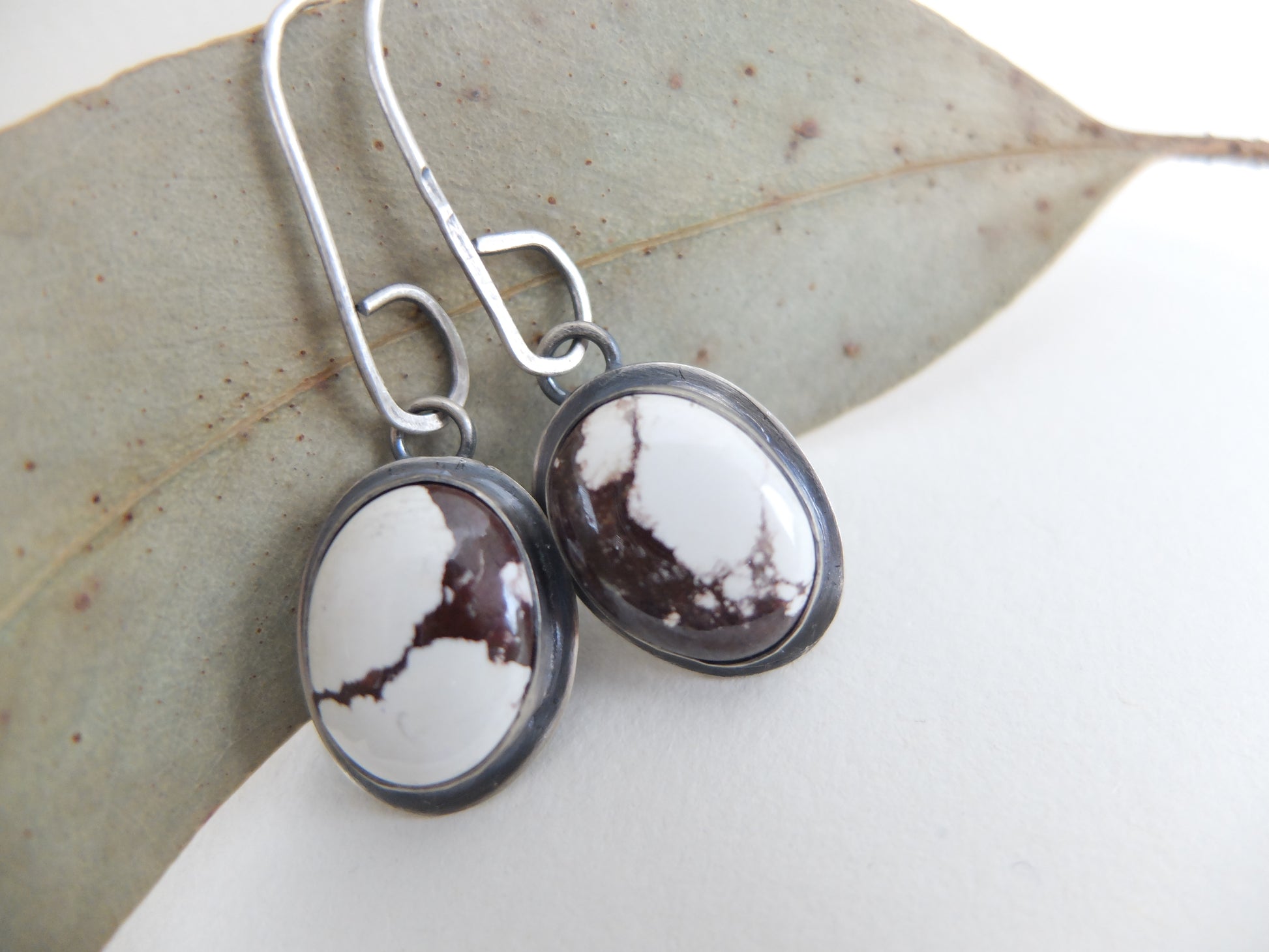 Silver earrings with oval gemstones on a leaf background