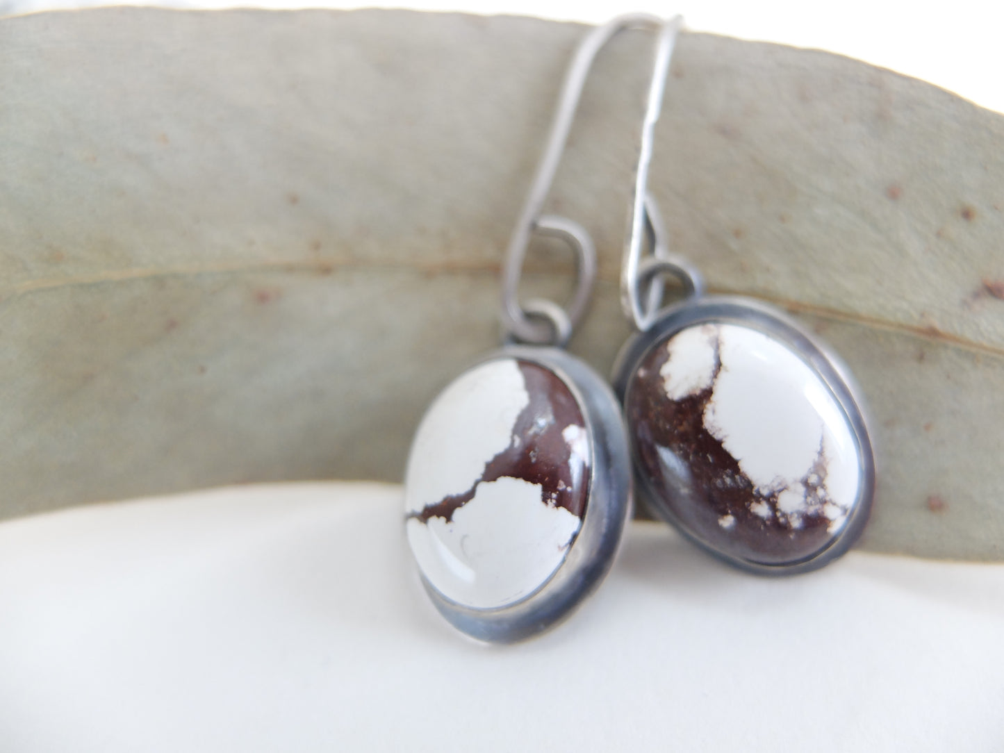 Silver earrings with white and brown stone on a light background
