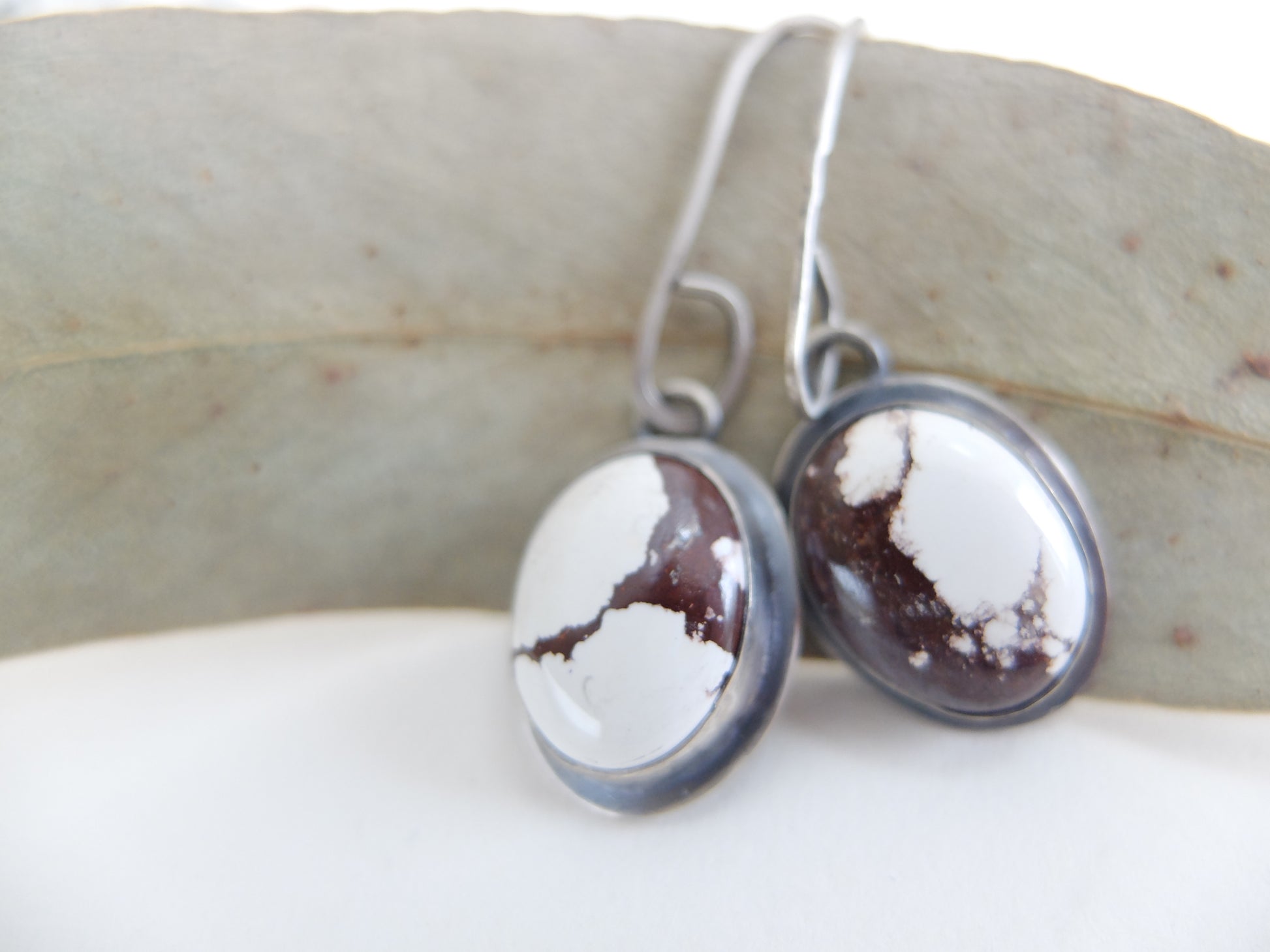 Silver earrings with white and brown stone on a light background