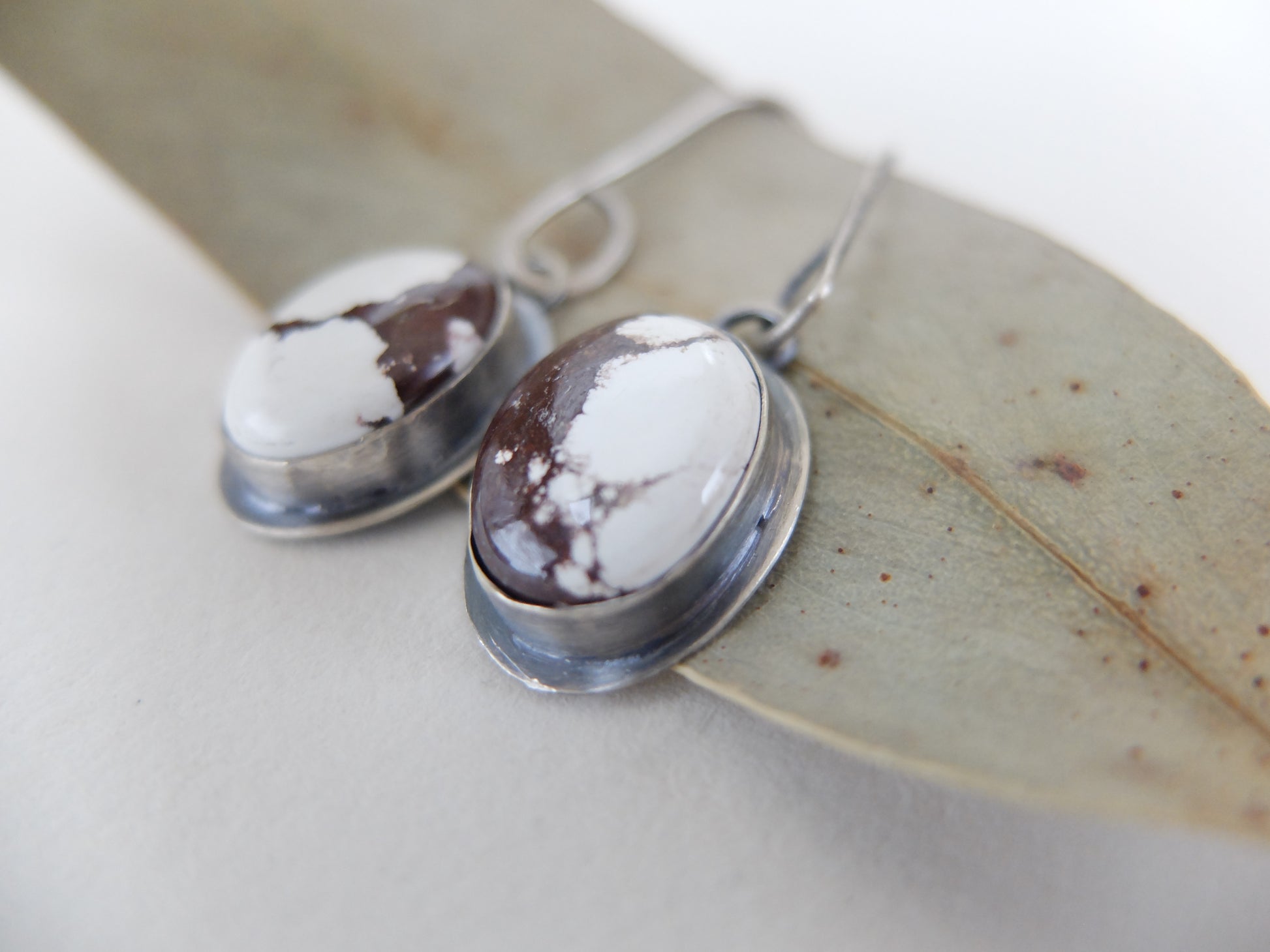 Pair of silver earrings with white and brown stone on a light background