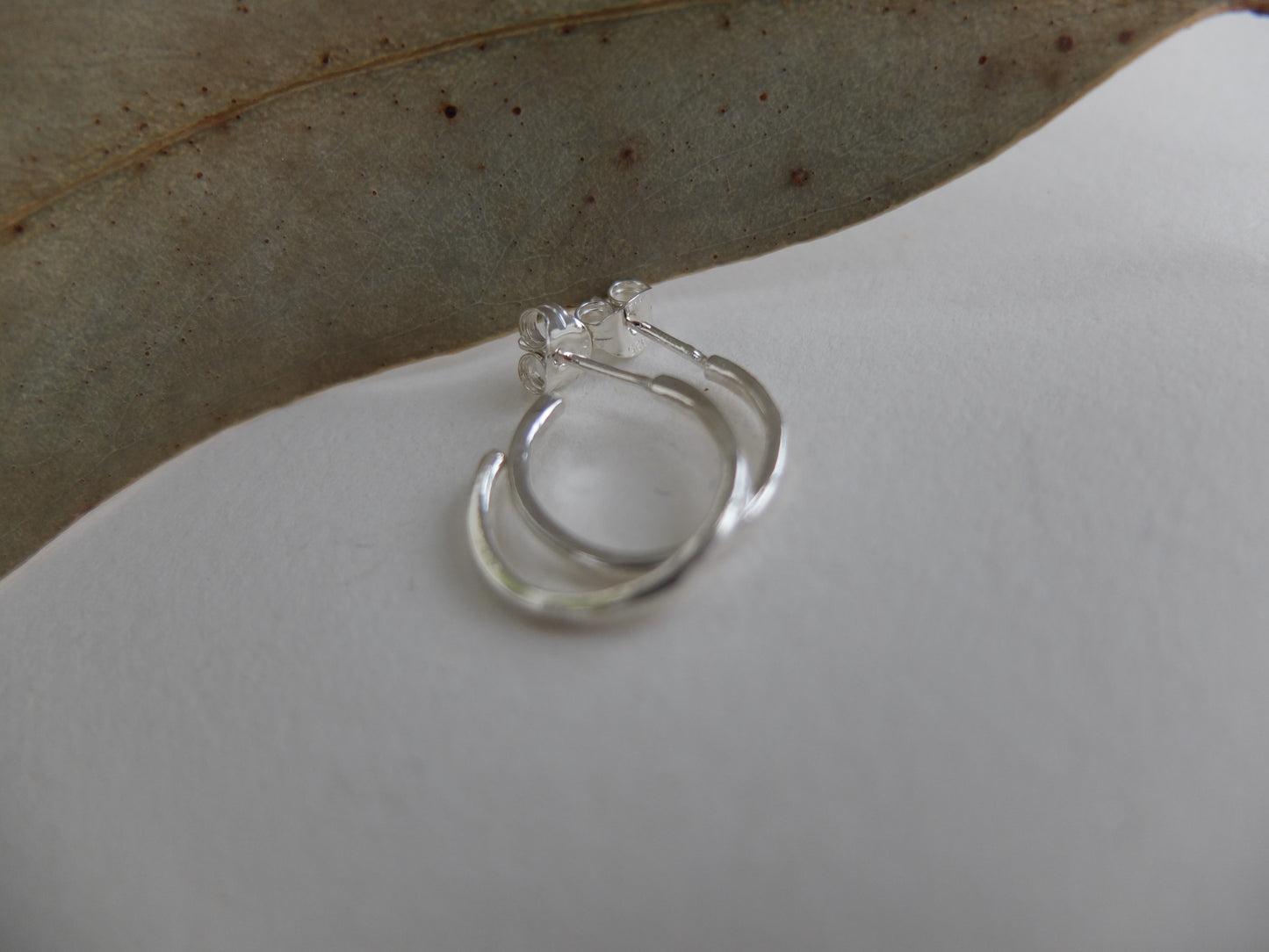 Silver hoop earrings on a white surface with a leaf in the background