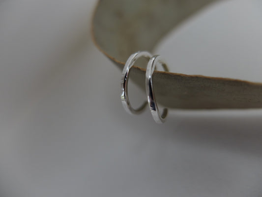 Two silver hoop earrings on a light wooden surface