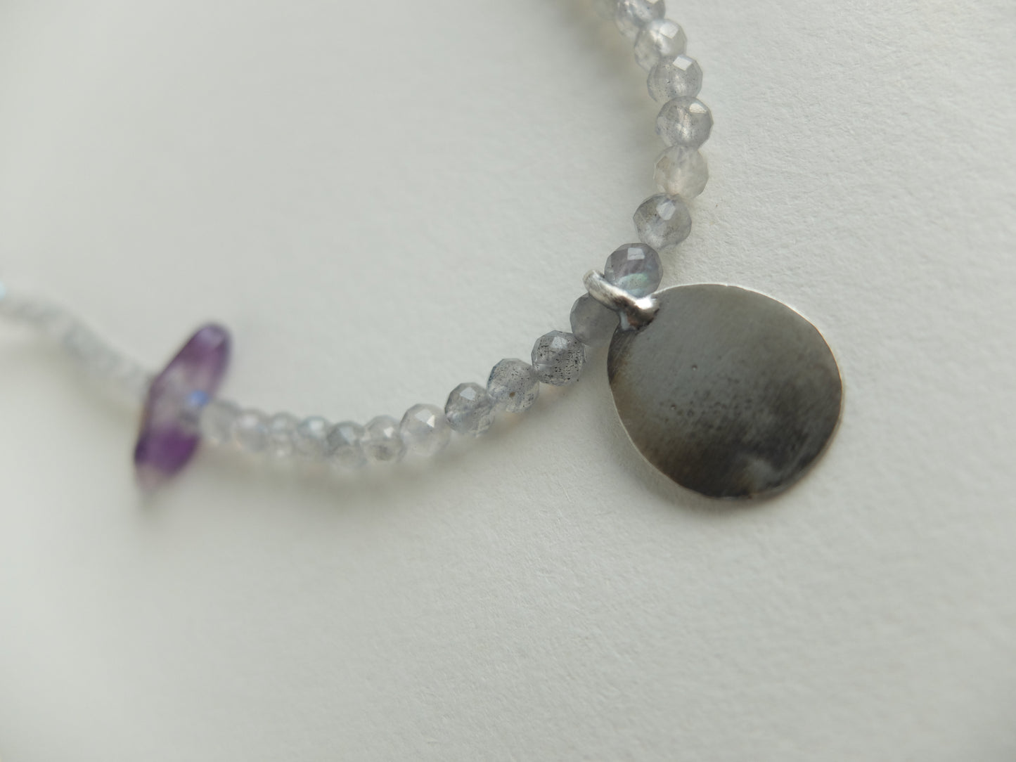 Necklace with small round silver pendant and beads on a light background