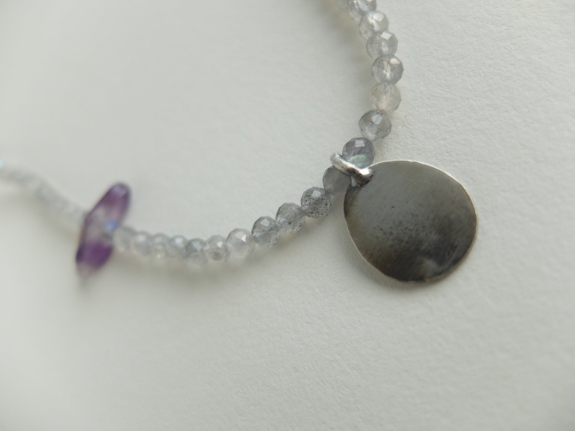 Necklace with small round silver pendant and beads on a light background