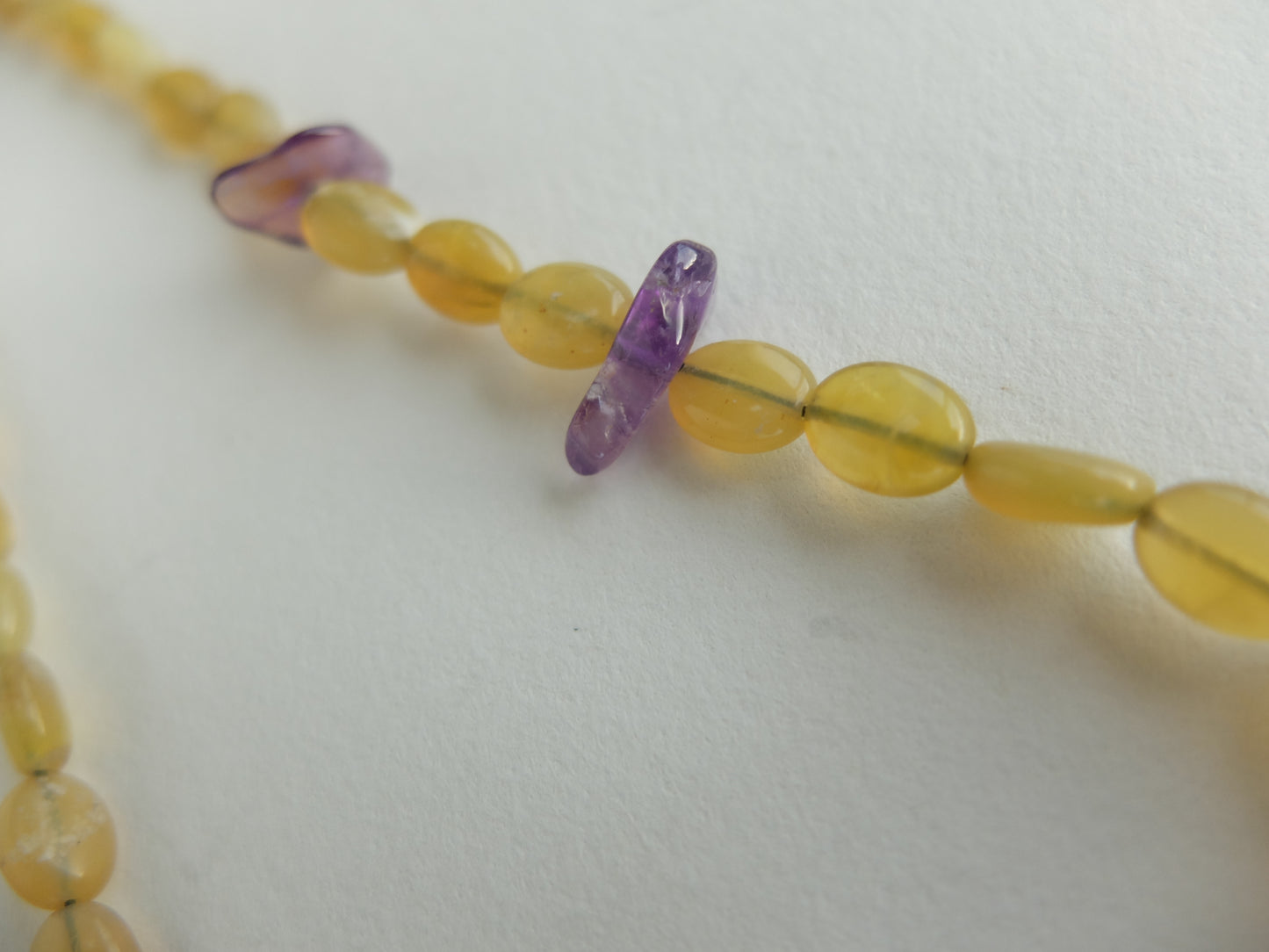 Close-up of amber and purple beaded necklace on a white background