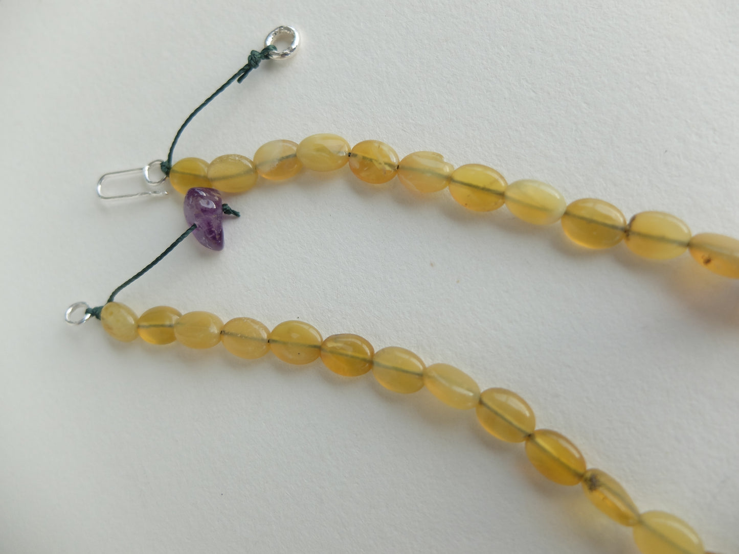 Beaded necklace with yellow beads and a purple heart pendant on a white background