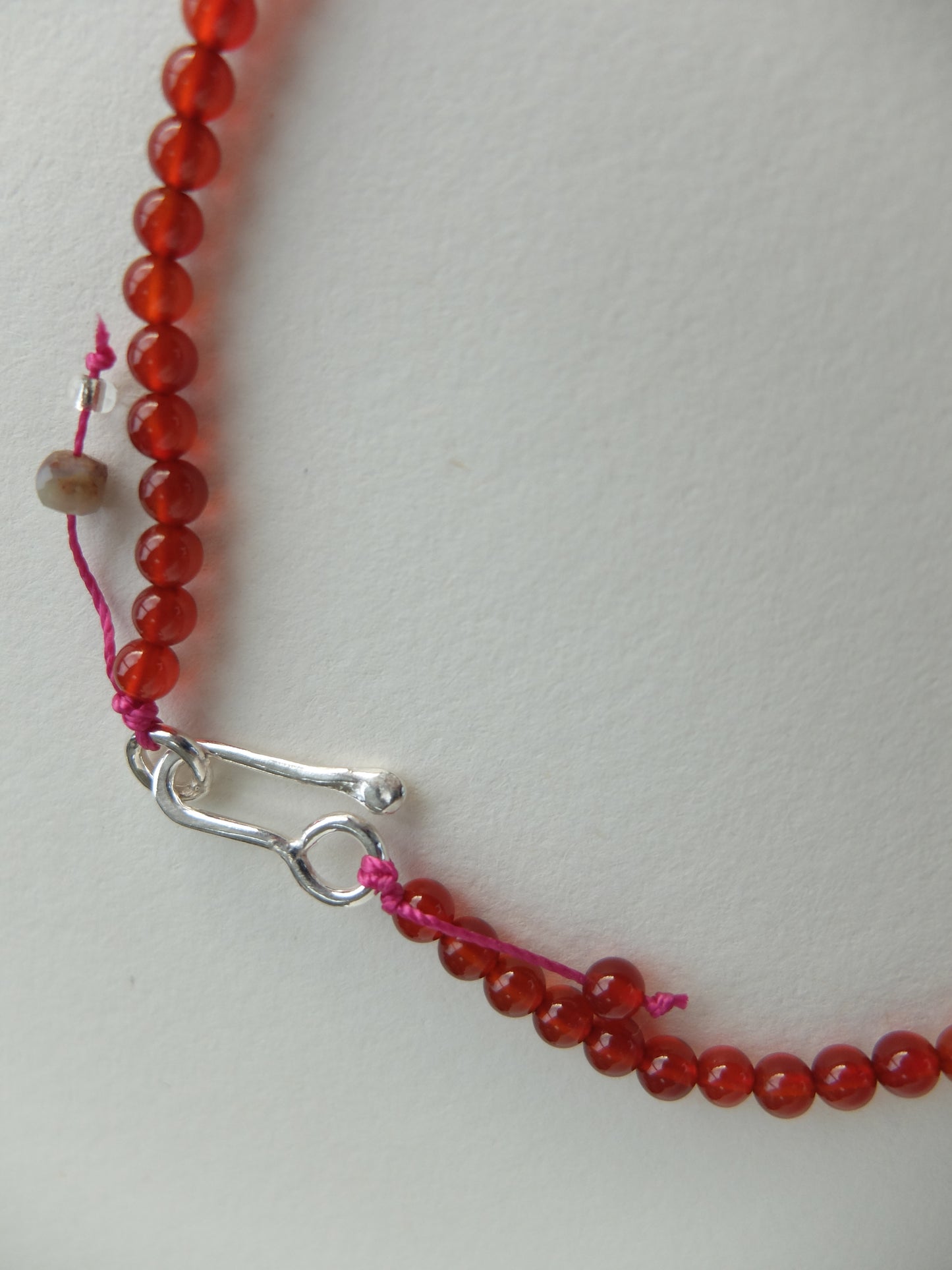Close-up of a red beaded necklace with a silver clasp on a light gray background