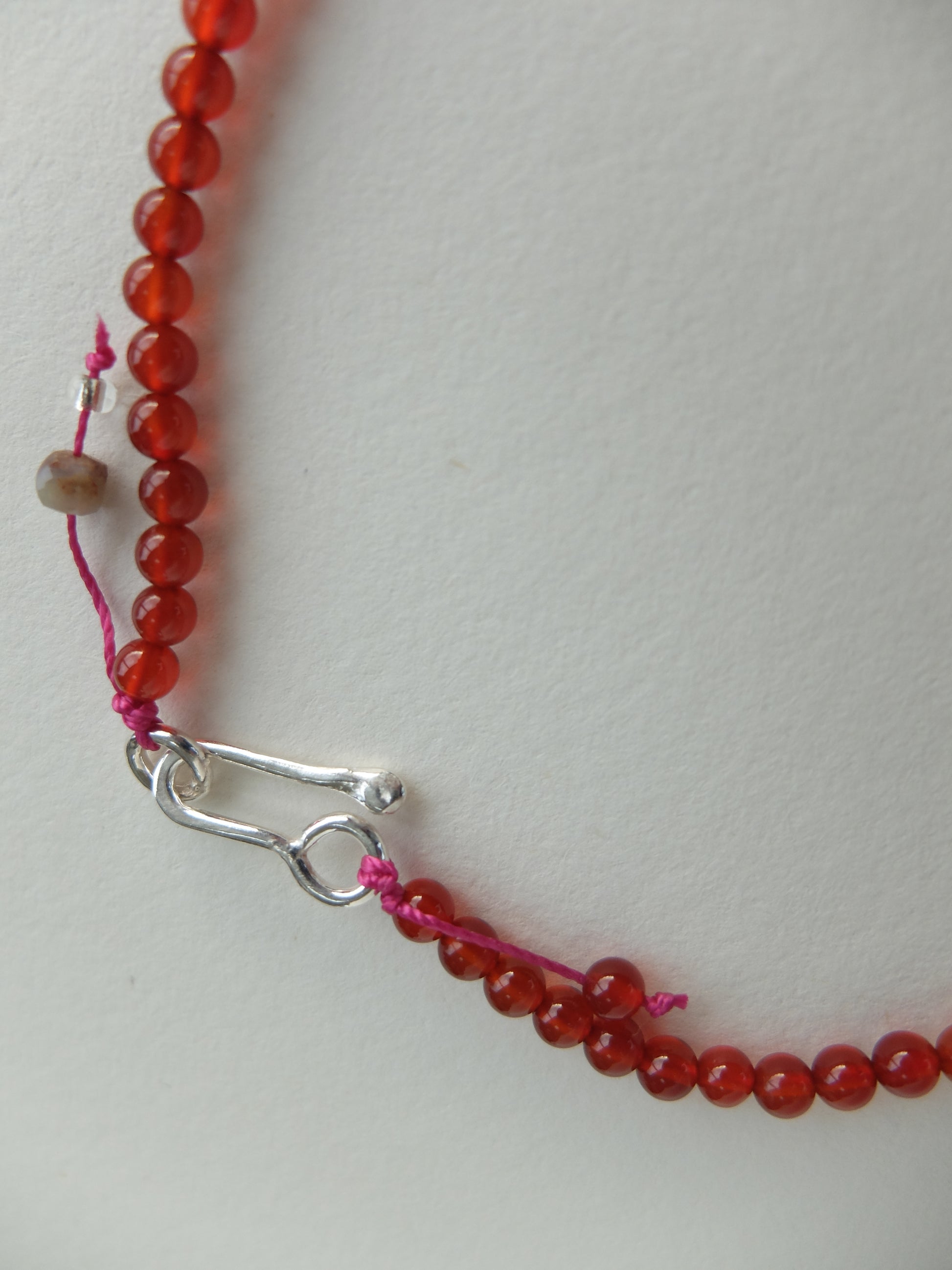Close-up of a red beaded necklace with a silver clasp on a light gray background