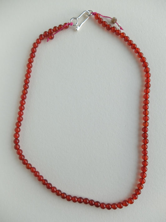 Red beaded necklace with a silver clasp on a light gray background