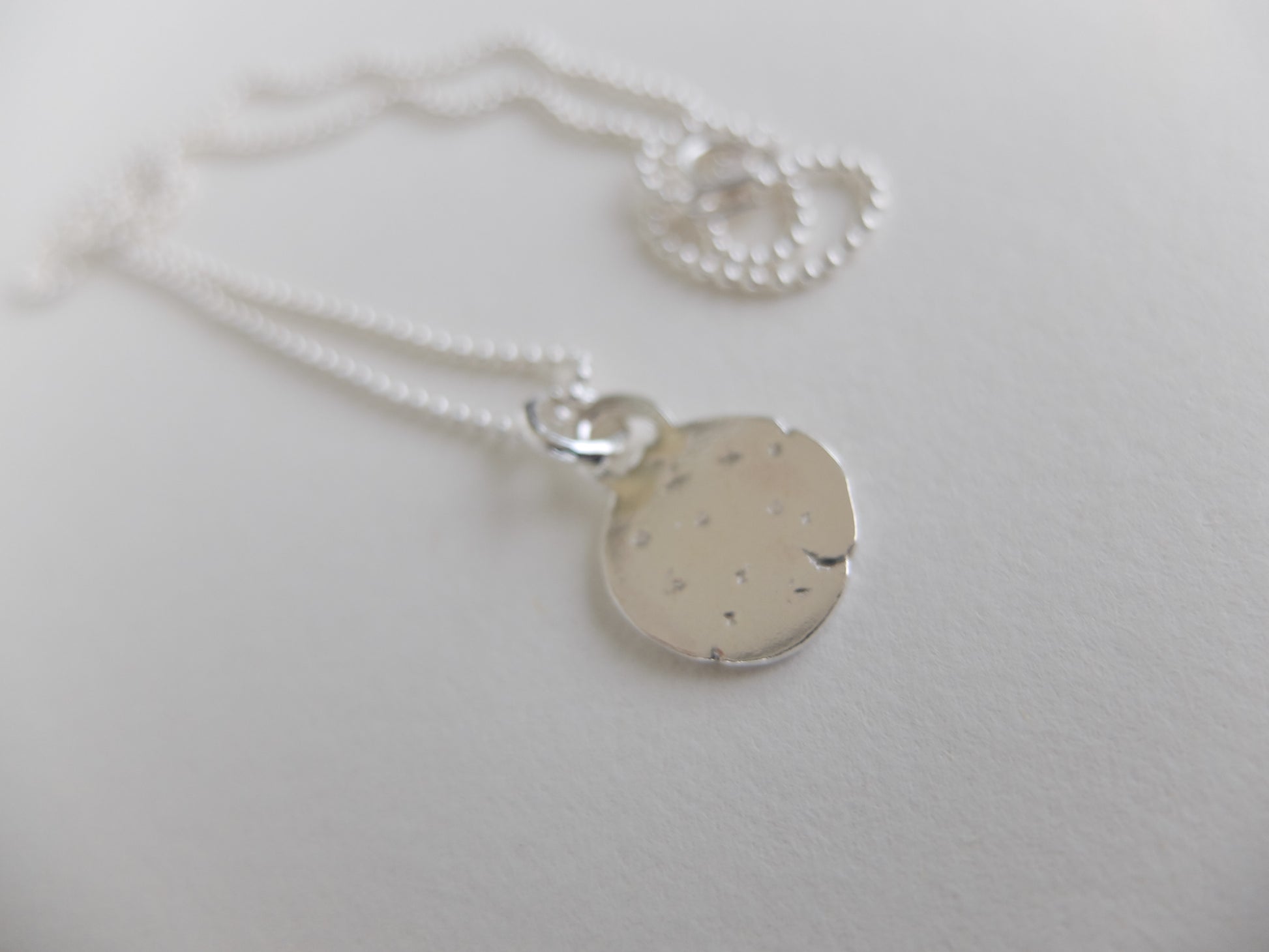 Silver necklace with a round pendant on a light gray background