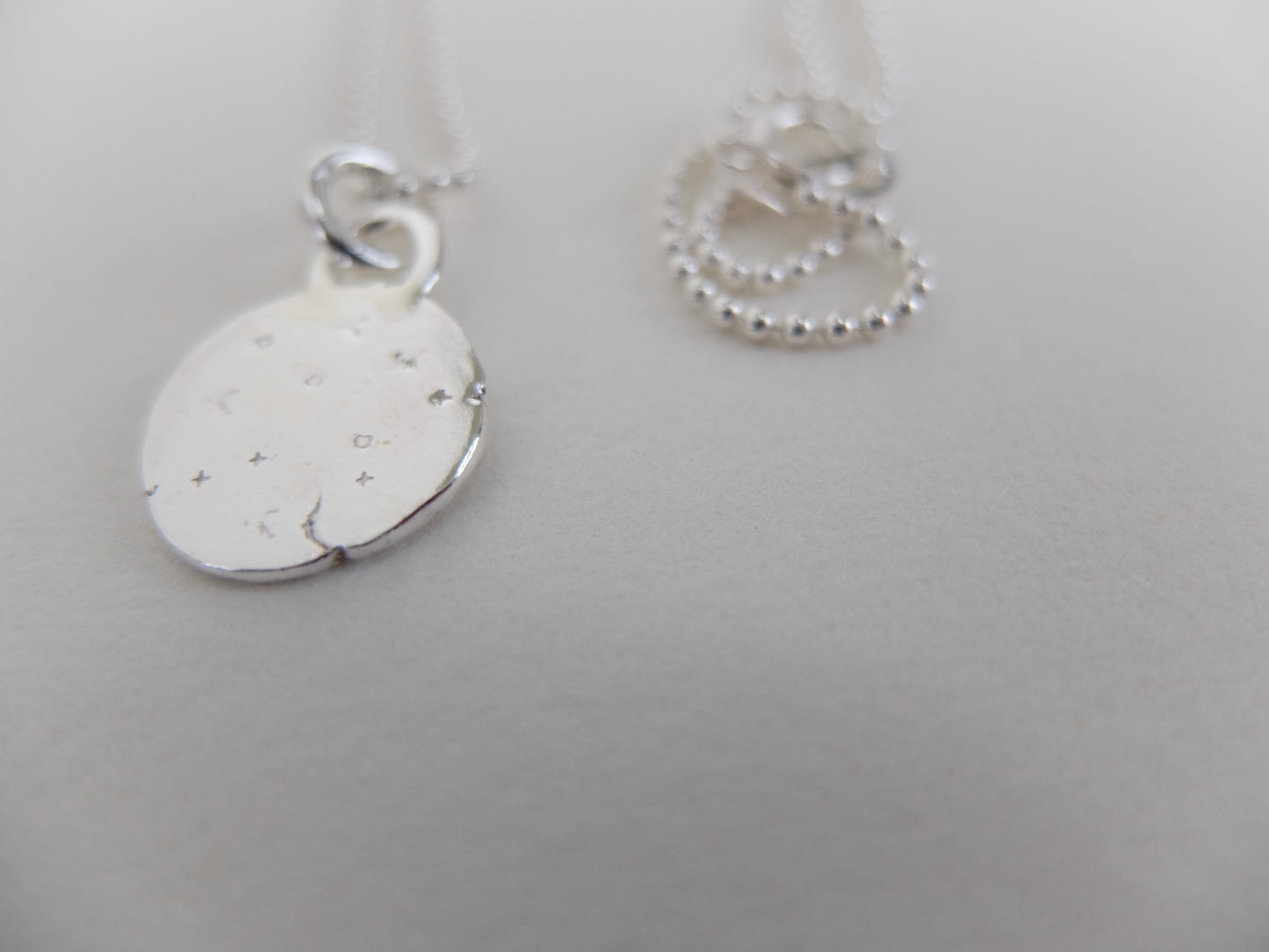 Silver necklace with a round pendant on a light gray background