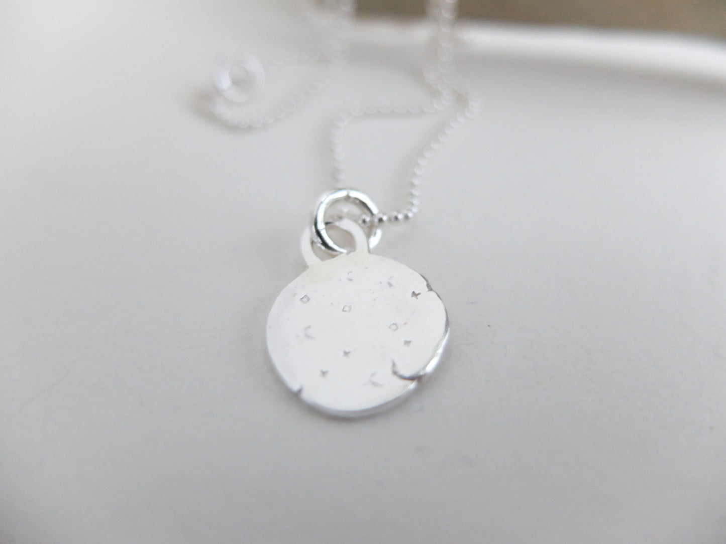 Silver necklace with a round pendant on a light gray background