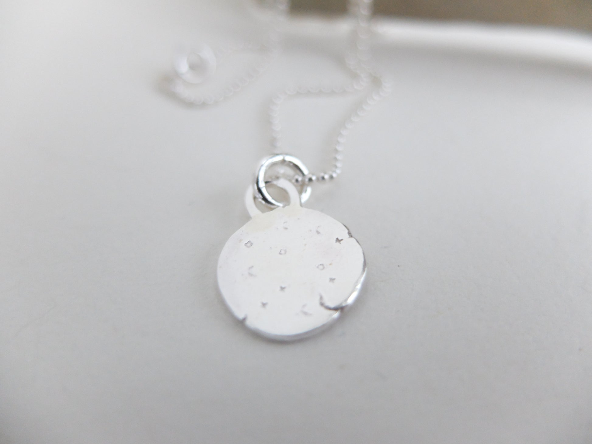 Silver necklace with a round pendant on a light gray background