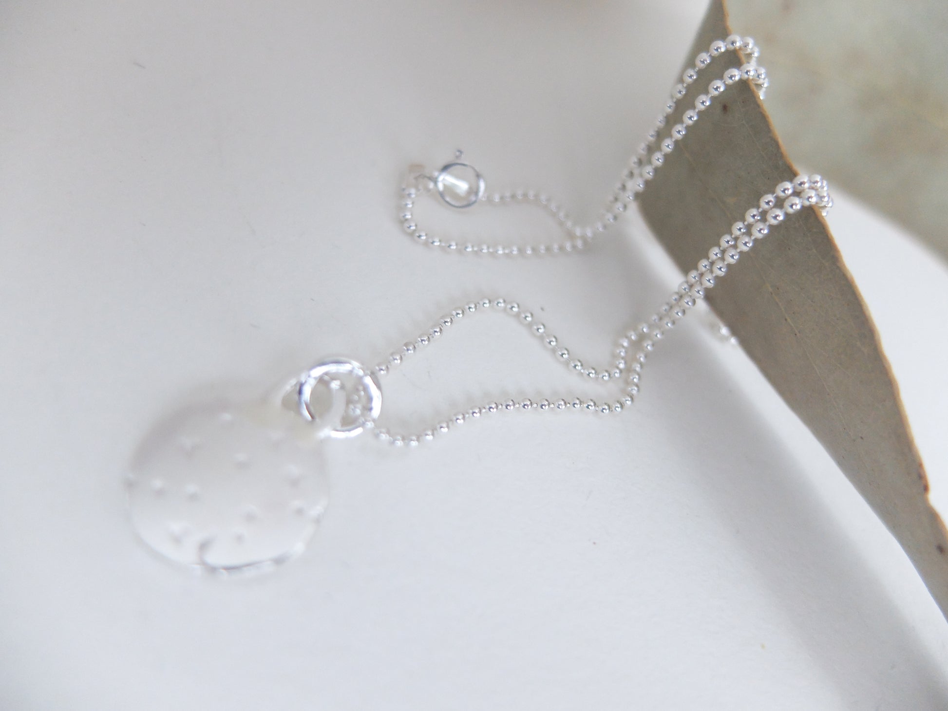 Silver necklace with a clear pendant on a white surface