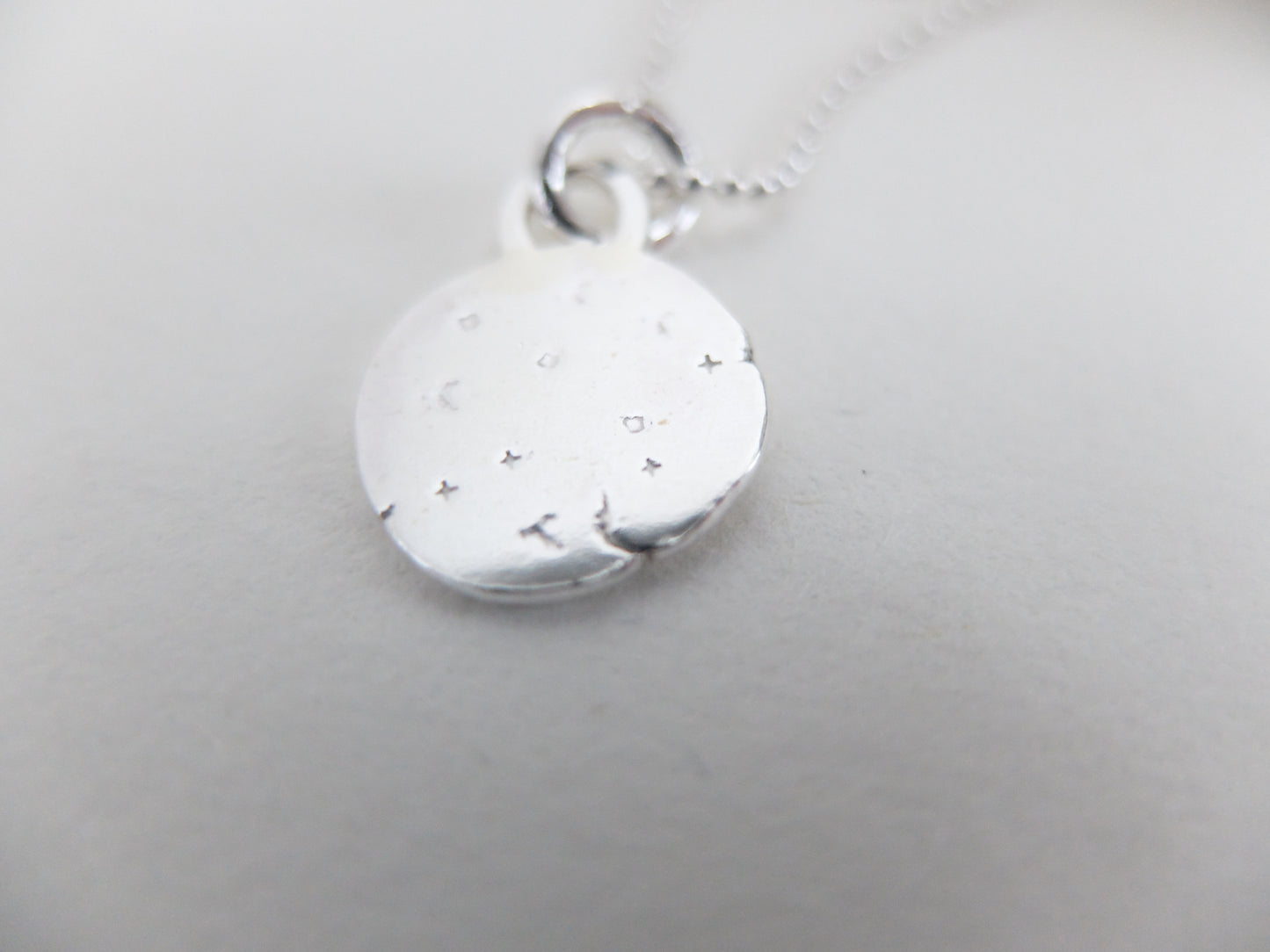 Silver pendant with engraved design on a light gray background