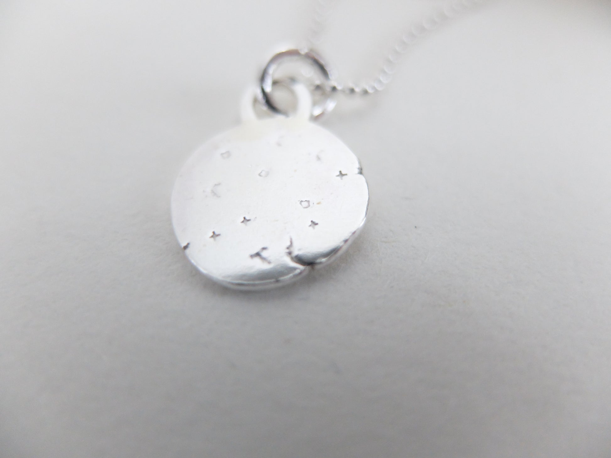 Silver pendant with engraved design on a light gray background